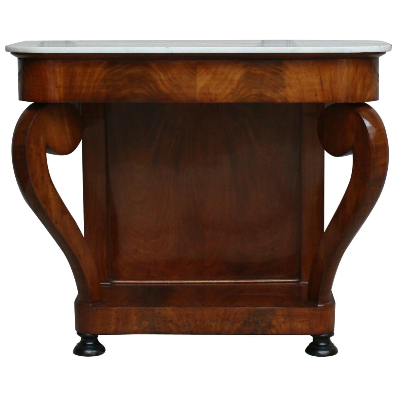 A antique French Louis-Philippe period mahogany veneer console from the mid-19th century with white marble top and 2 round black ebonized feet. Dovetailed wood construction. 
The console table is professionally re-polished by hand with shellac