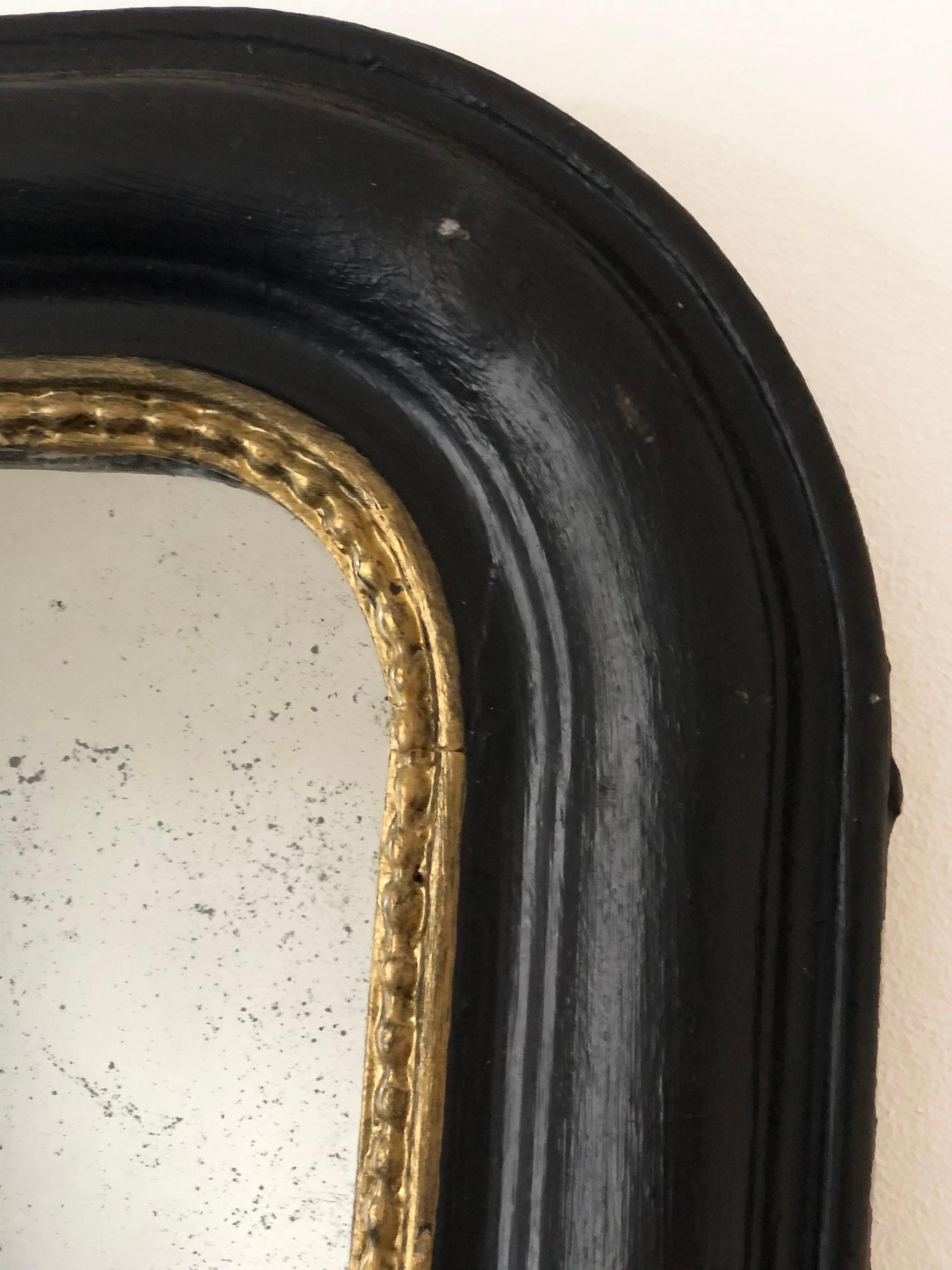 An enchanting original Louis Philippe mirror from France, dating to the late 19th century. The mirror features a refined black frame with a gold pearl rim, mercury glass, and a gracefully curved top, exuding timeless elegance and charm.

Object: