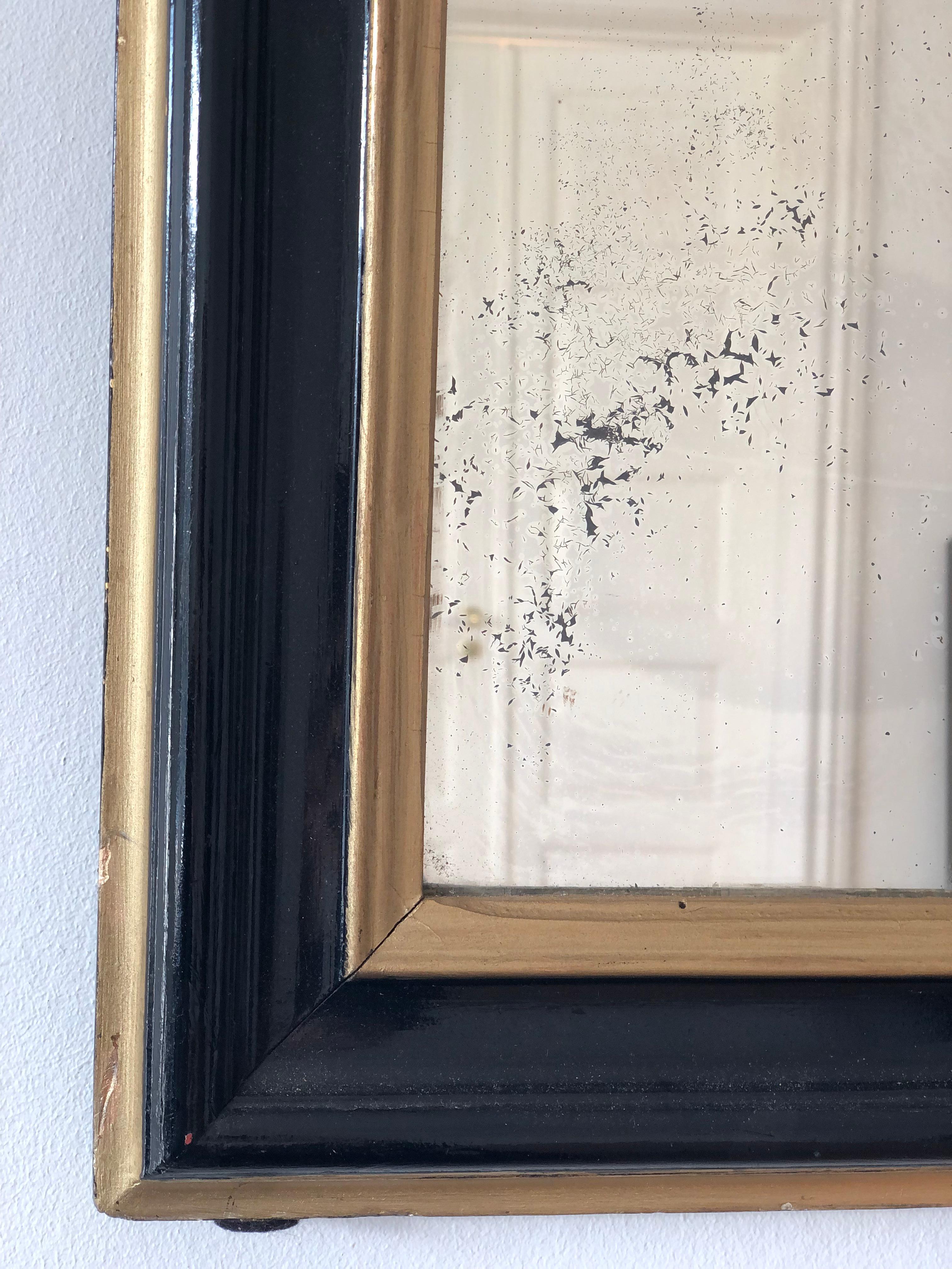 An enchanting original Louis Philippe mirror from France, dating to the late 19th century. The mirror features a refined black frame with a soft gold trim, mercury glass, and a gracefully curved top, exuding timeless elegance and charm.

Object: