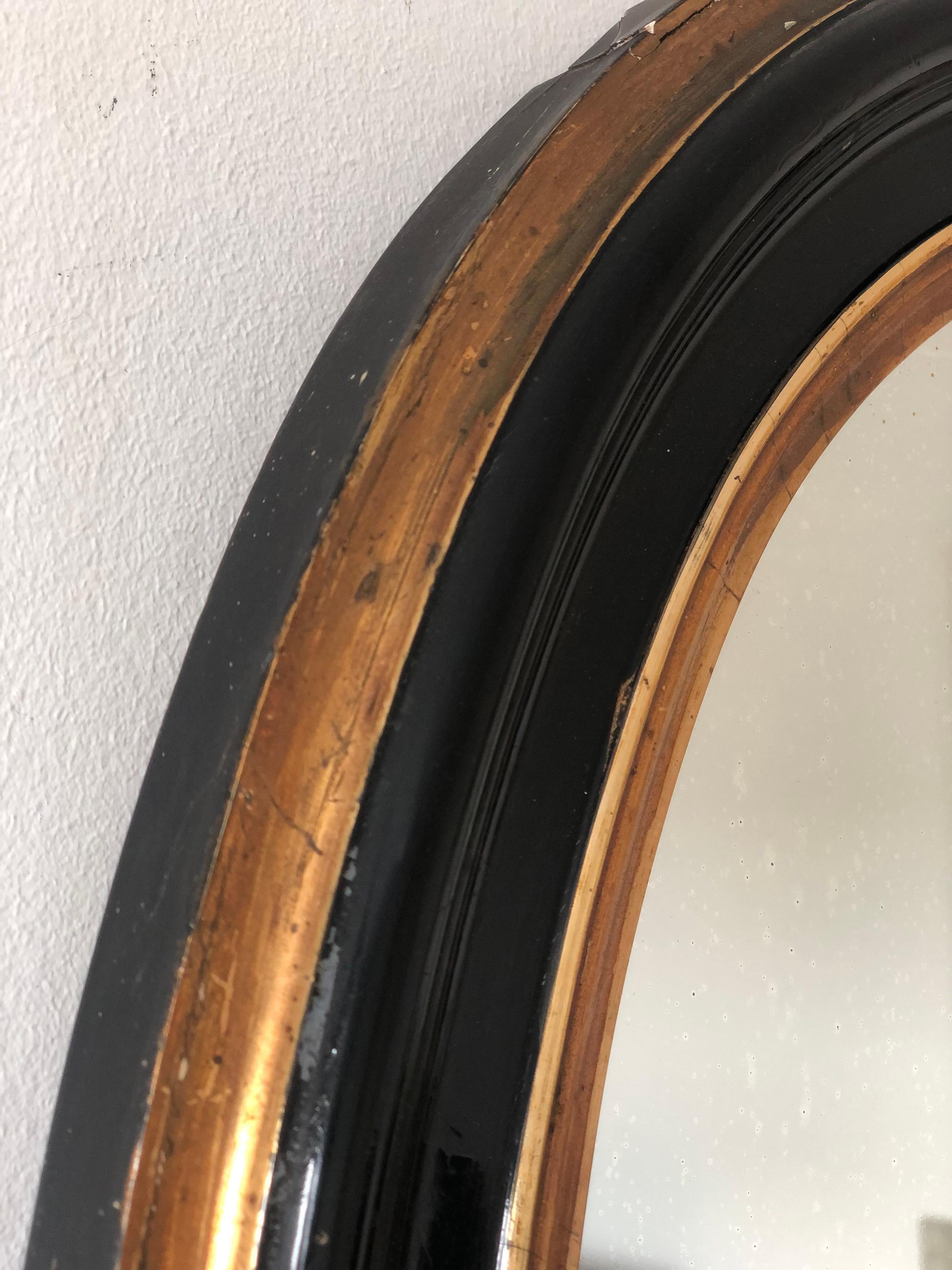 An enchanting original Louis Philippe mirror from France, dating to the late 19th century. The mirror features a refined black frame with a soft gold trim, mercury glass, and a gracefully curved frame, exuding timeless elegance and charm.

Object: