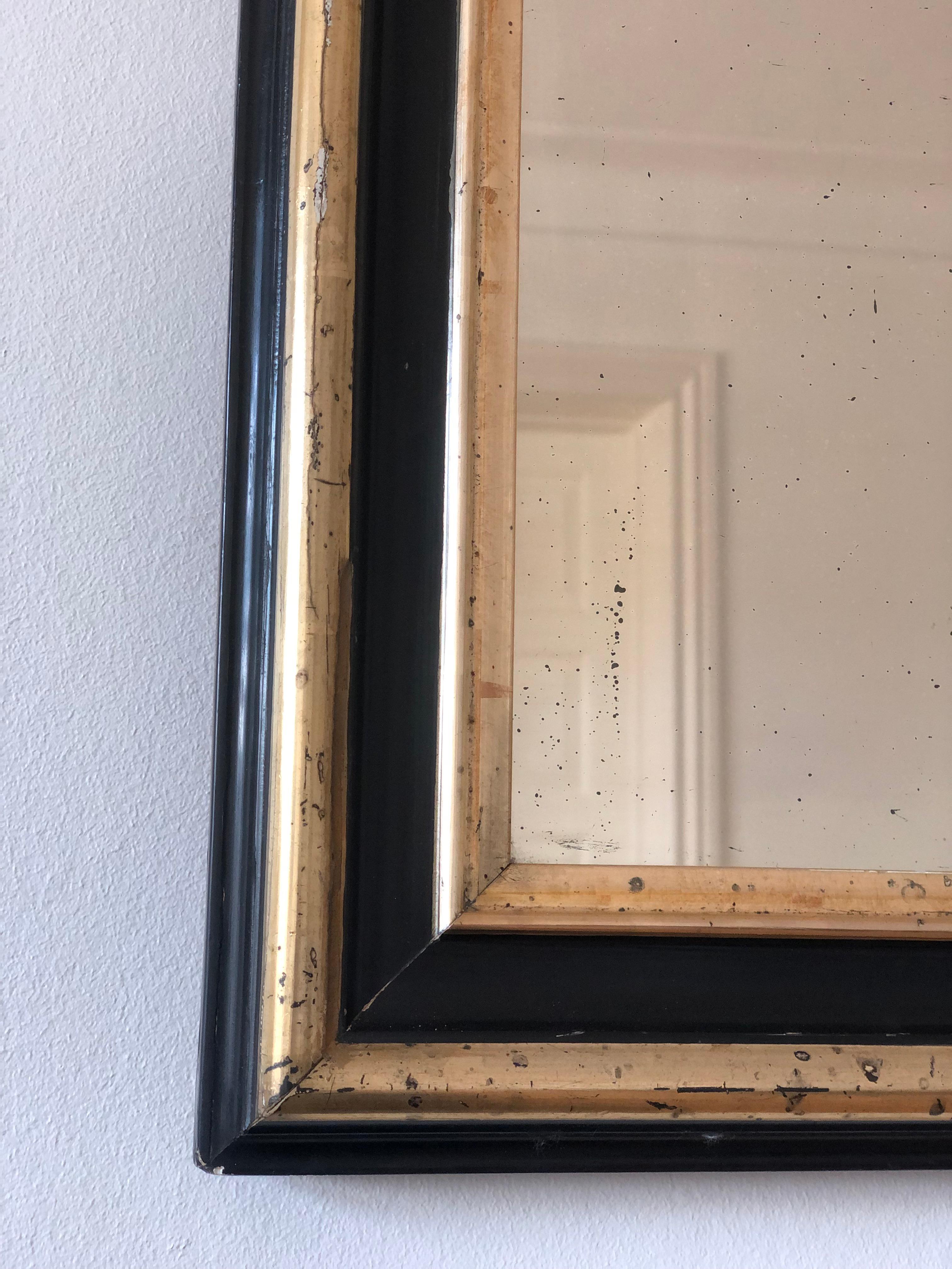 An enchanting original Louis Philippe mirror from France, dating to the late 19th century. The mirror features a refined black frame with a soft gold trim, mercury glass, and a gracefully curved top, exuding timeless elegance and charm.

Object: