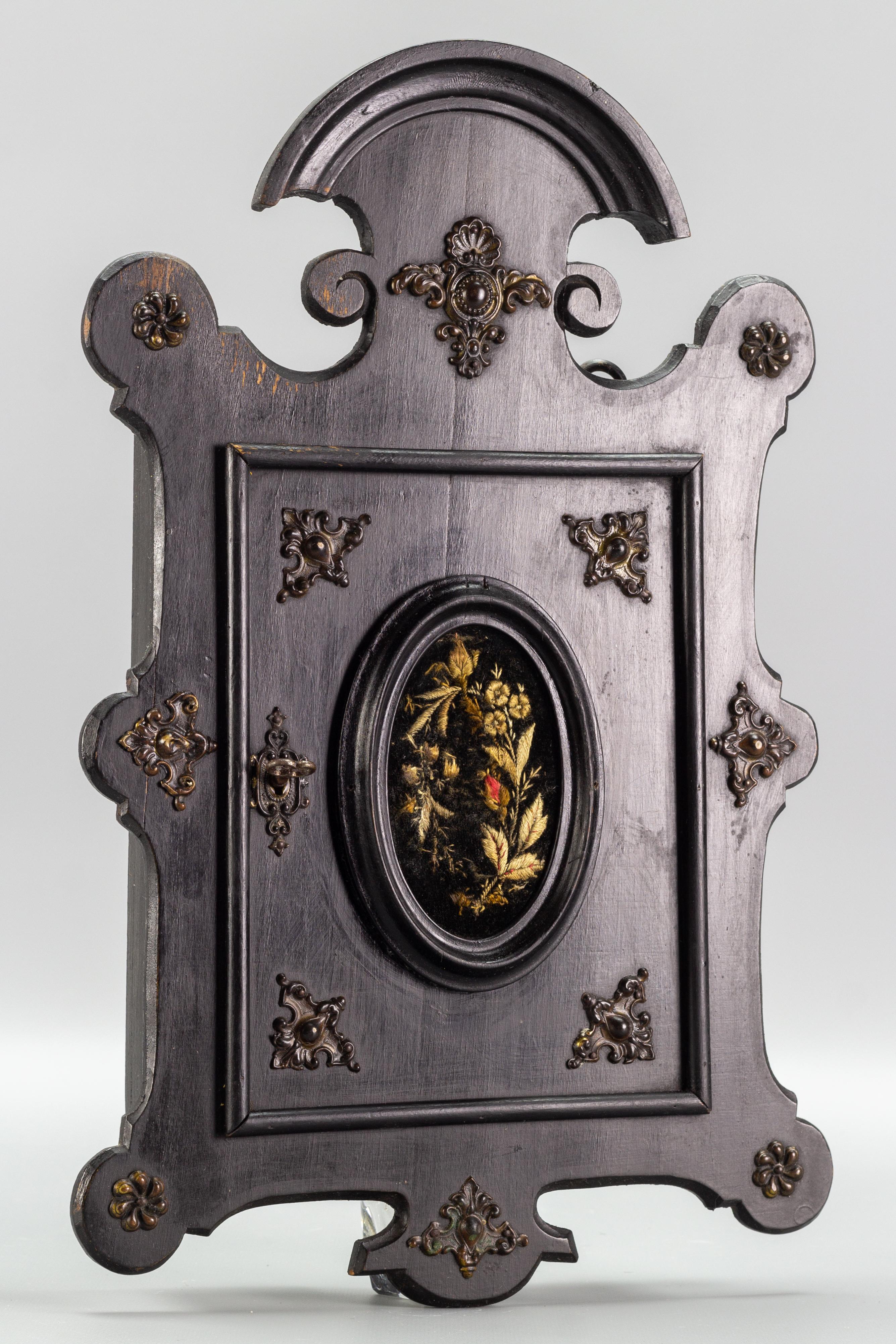 Antique Louis Philippe style black wooden wall hanging key cabinet, ca 1890.
An ornate wall-hanging key cabinet with beautiful brass decorative mounts. This wall cabinet features one door with central embroidery, opening to reveal eight metal hooks