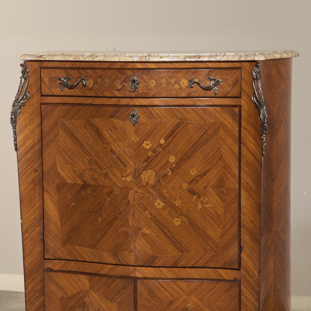 Crafted from exotic imported mahogany with precisely oriented grain patterns, this secretary features floral and foliate marquetry on the upper drawer; drop front desk surface and lower cabinet doors. Contoured cornerposts have been adorned with