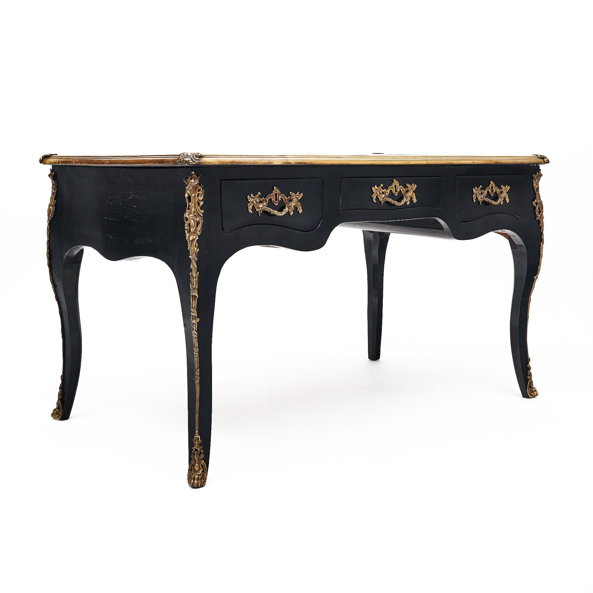 Bureau ancien de style Louis XV en bois de rose ébénisé et recouvert d'un vernis lustré de qualité muséale. Le bureau est doté d'un plateau en cuir marron d'origine, orné d'une frise en feuilles d'or. Trois tiroirs à queue d'aronde sont richement