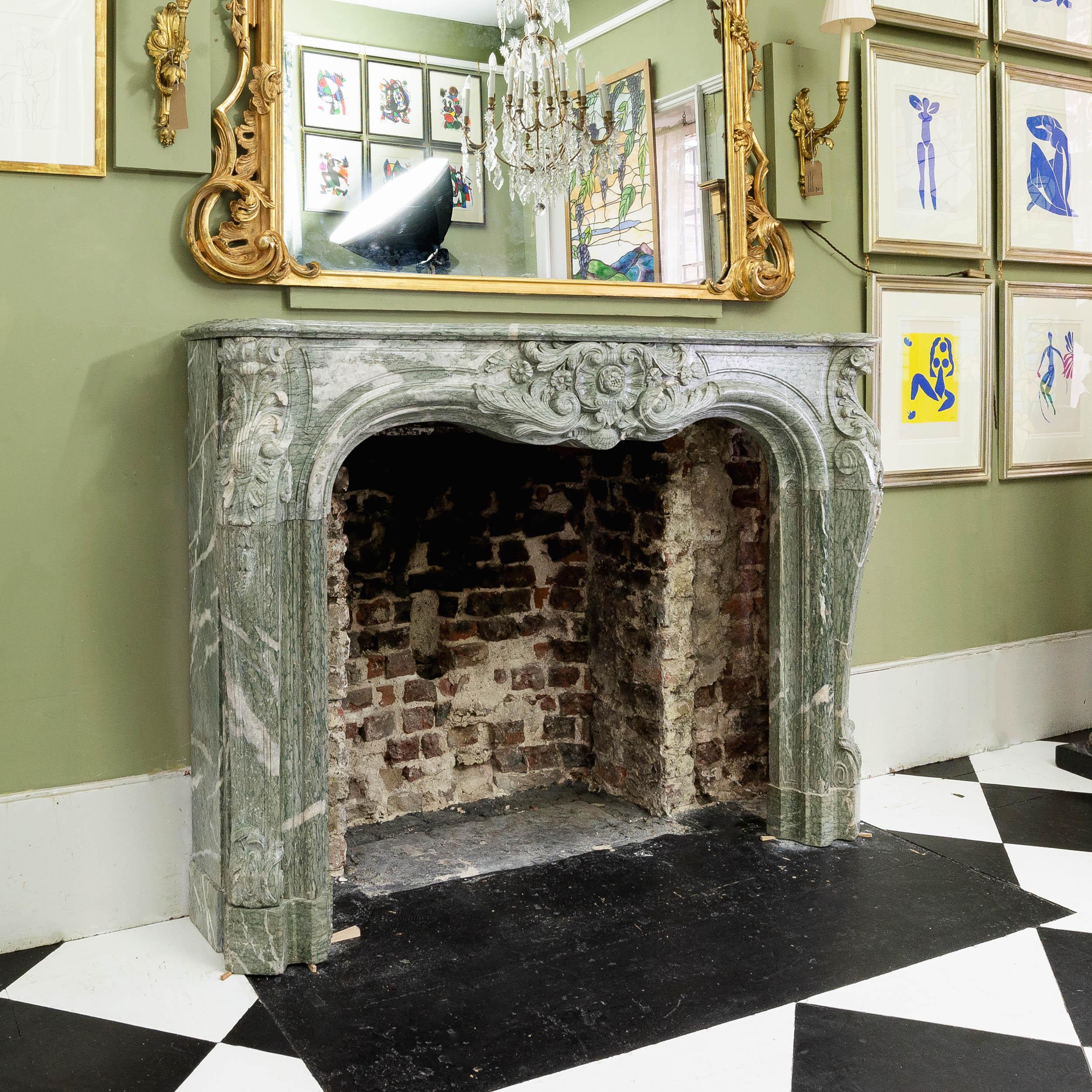An antique Louis XV Campan Vert fireplace, the boldly shaped and moulded shelf above frieze with double scallop shell cartouche with central flower head, the canted jambs headed by acanthine fronds with trails of bellflowers below, on shaped block