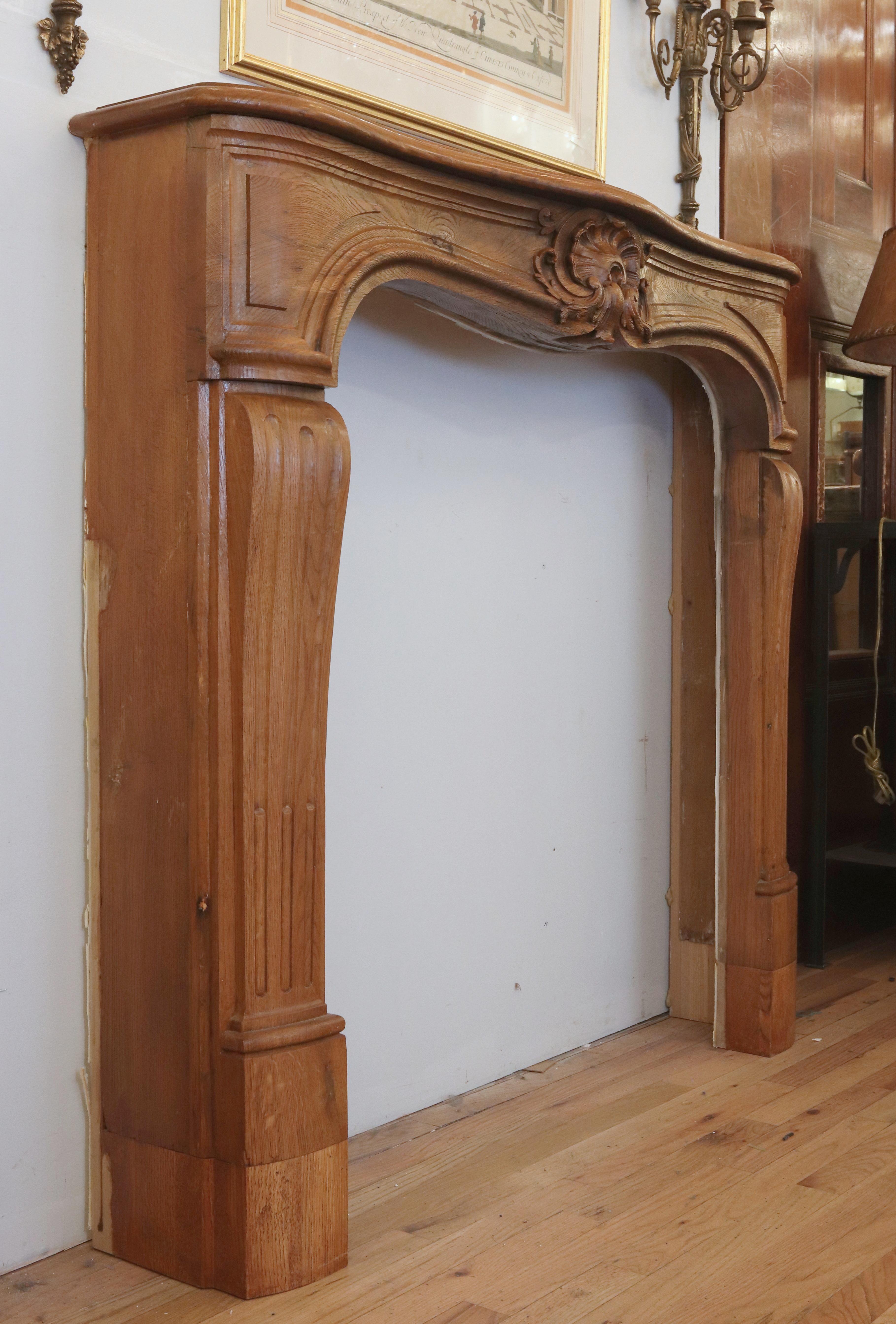 Antique Louis XV style fireplace mantel made of oak with dark wood tone finish. It features a centered carved shell motif and a black marble surround. Good condition with appropriate wear from age. One available. Please note, this item is located in