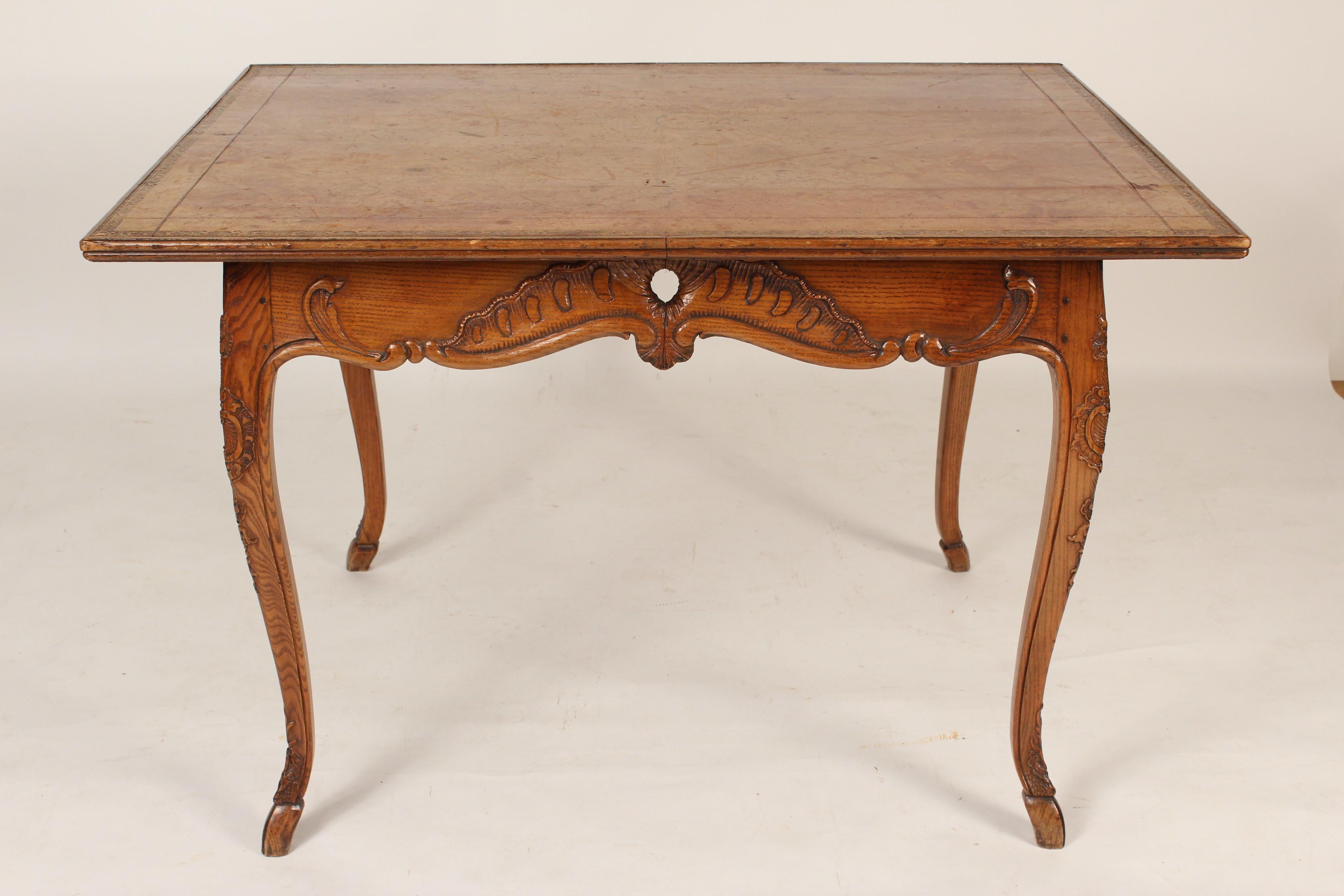 Antique Louis XV provincial style leather top writing / games table, late 19th century. With an old tooled leather top, carved aprons, with carved c scrolled cabriole legs ending in hoof feet. Height from bottom of apron to floor 22.75