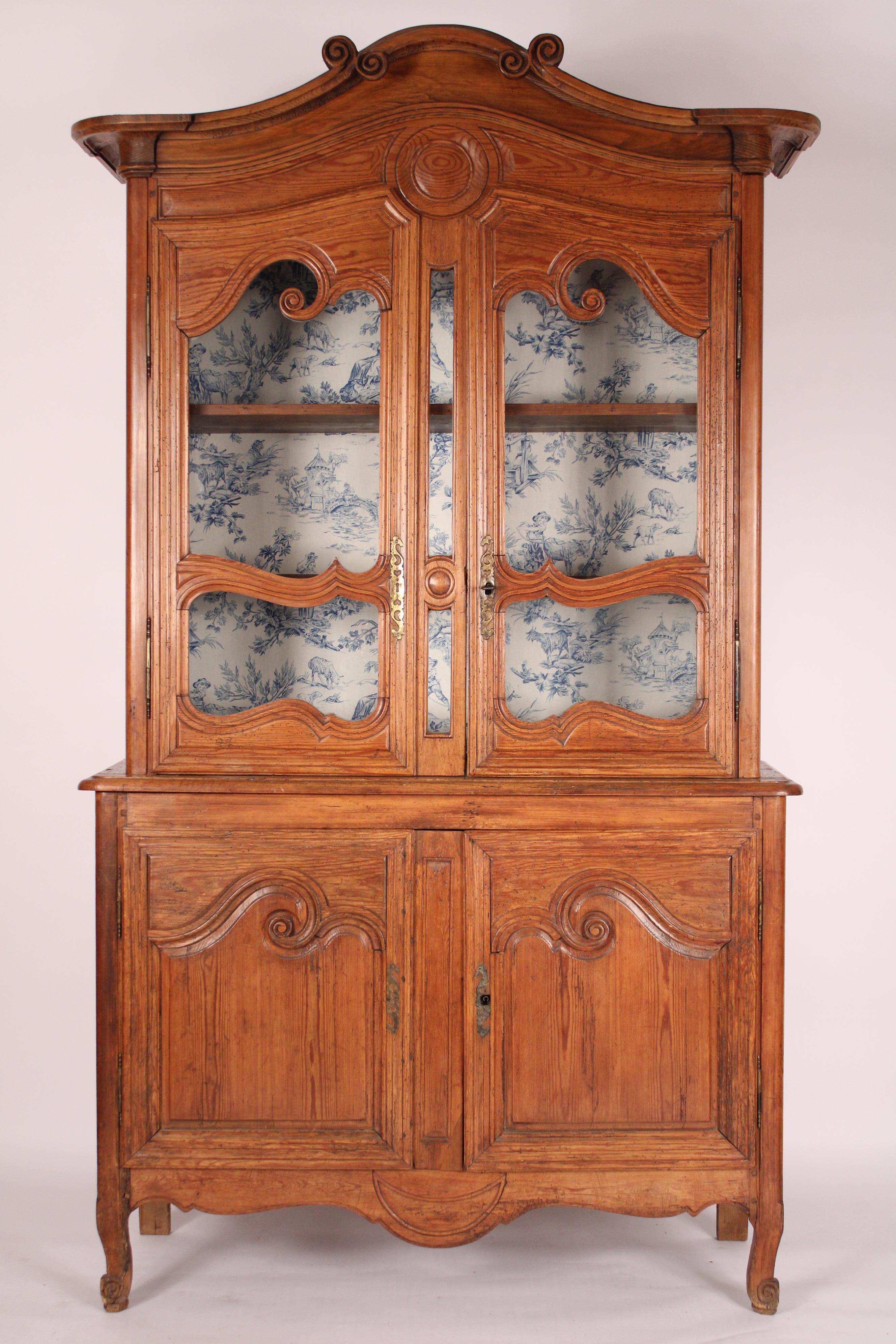 Antico buffet au deux corps in pino in stile Luigi XV, XIX secolo. La parte superiore è caratterizzata da un doppio frontone rimovibile a forma di serpentina che sovrasta due porte in vetro con scure in ottone, l'interno foderato con tessuto toile