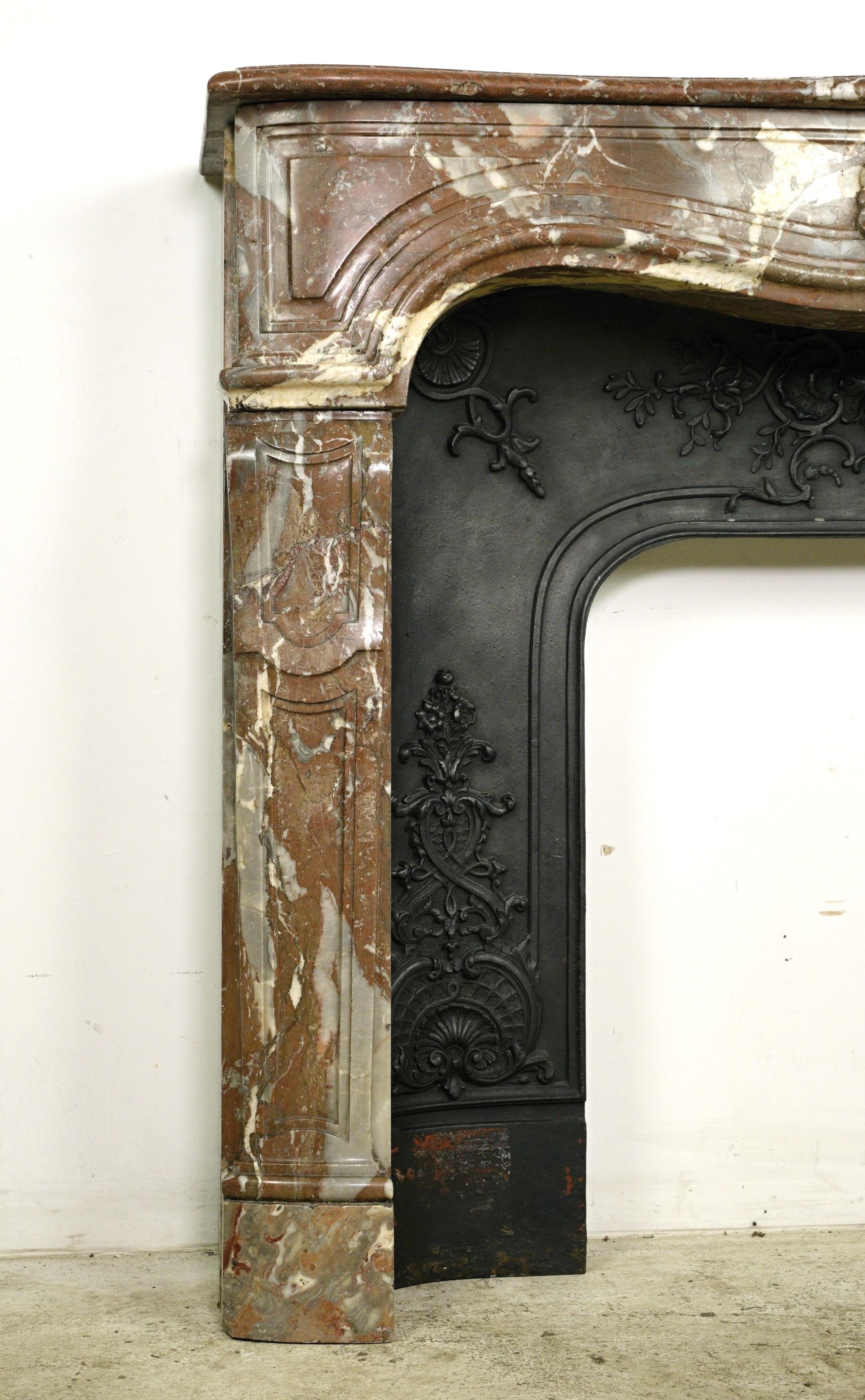 This piece was procured from an esteemed estate located in Greenwich, Connecticut. This rouge royale marble mantel features a serpentine design, showcasing unique and antique carvings. While the mantel itself is in good condition, with some minor