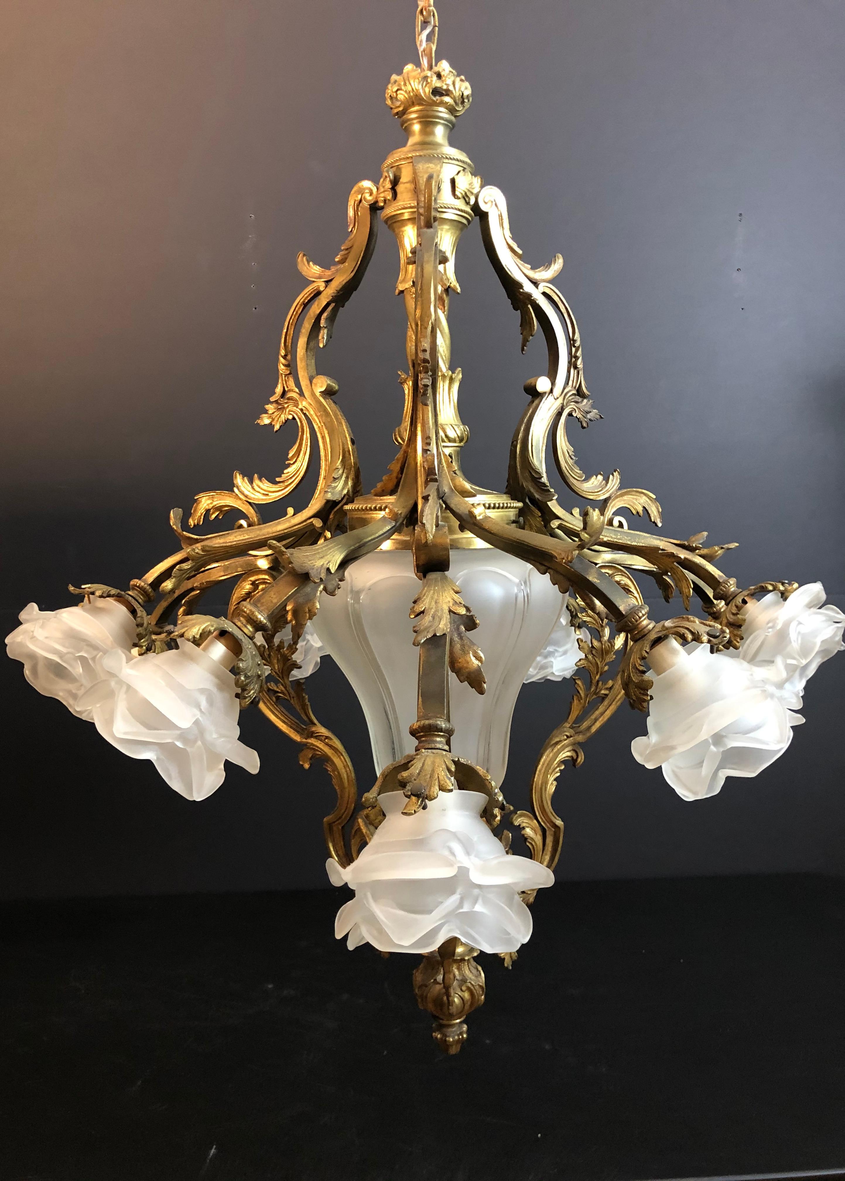 Antique  Louis XV style bronze chandelier with a Rococo influence. Frosted glass rose bud shades on nine scrolled arms with foliate details. Center frosted glass shade conceals additional light. Total of 10 lights.