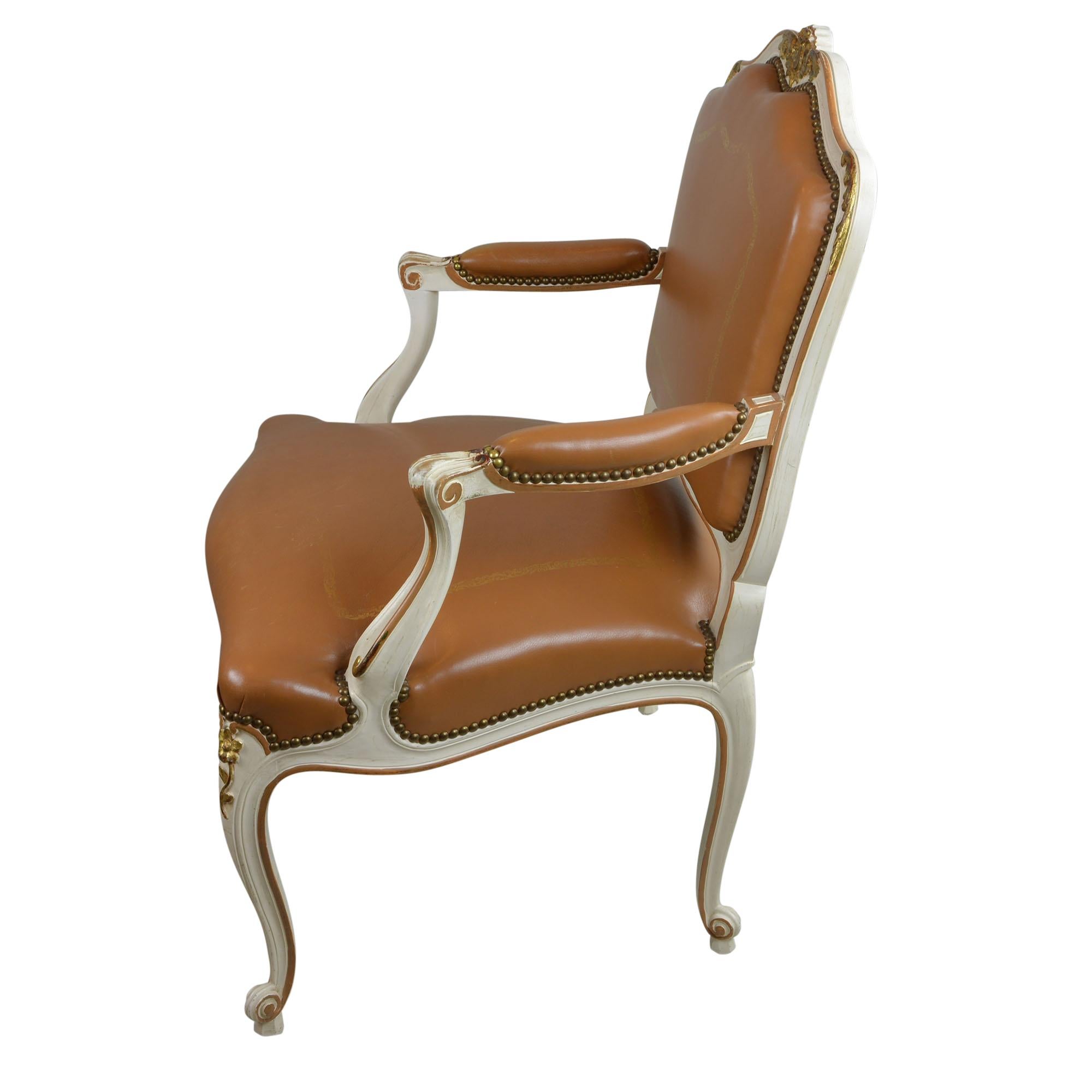 Lovely Louis XV style chair is upholstered in a saddle brown antique leather that is embellished with hand tooled gilt detailing. The chair has a frame that is painted in a creamy ivory color that has patinated over time, acquiring an amazing