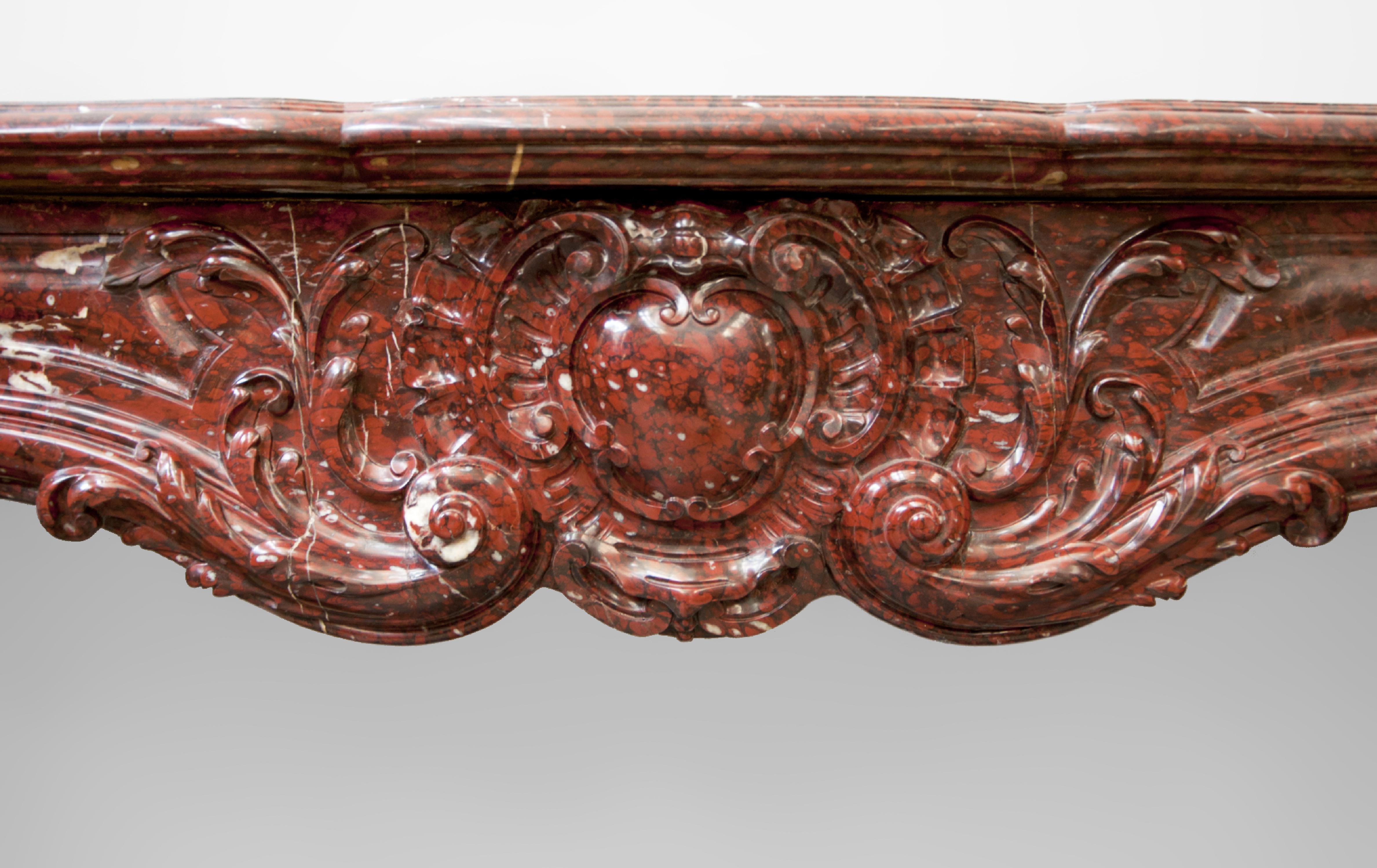 This beautiful antique Louis XV style fireplace was made out of Red Griotte marble during the 19th century. Extremely curved and decorated with fleshy sculptures, this fireplace is made in one of the finest French marbles, Red Griotte whose career
