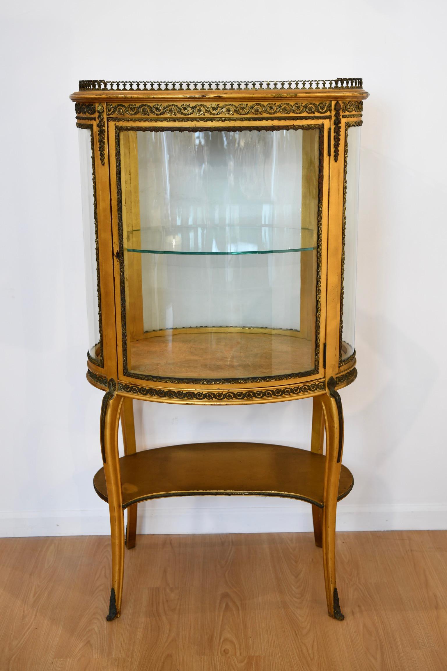 Antique Louis XV style large gilt vitrine or curio with curved glass and bronze mounts. The top is lined with a bronze gallery rail and curio comes with one glass shelf, a fabric lined bottom, and outside lower shelf. Key missing.