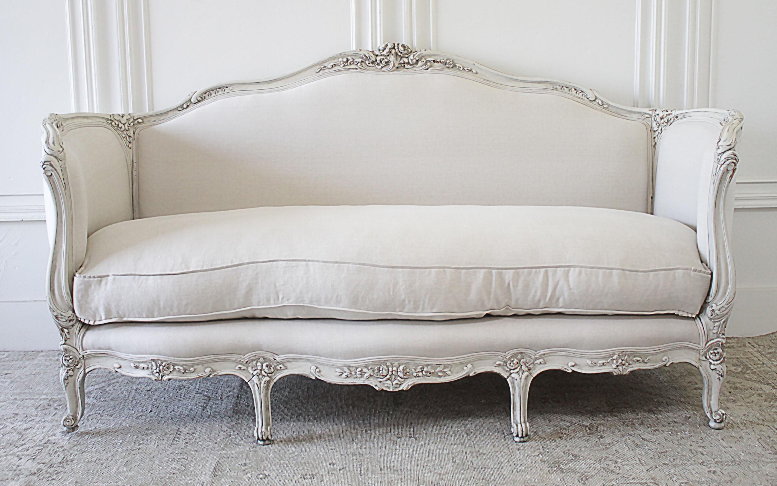 Antique Louis XV Style Painted and Upholstered French Sofa in Belgian Linen
This sofa has been painted in a soft oyster white finish, with subtle distressed edges, and antique patina.  Beautiful large carved roses,  curved side arms,  and large down