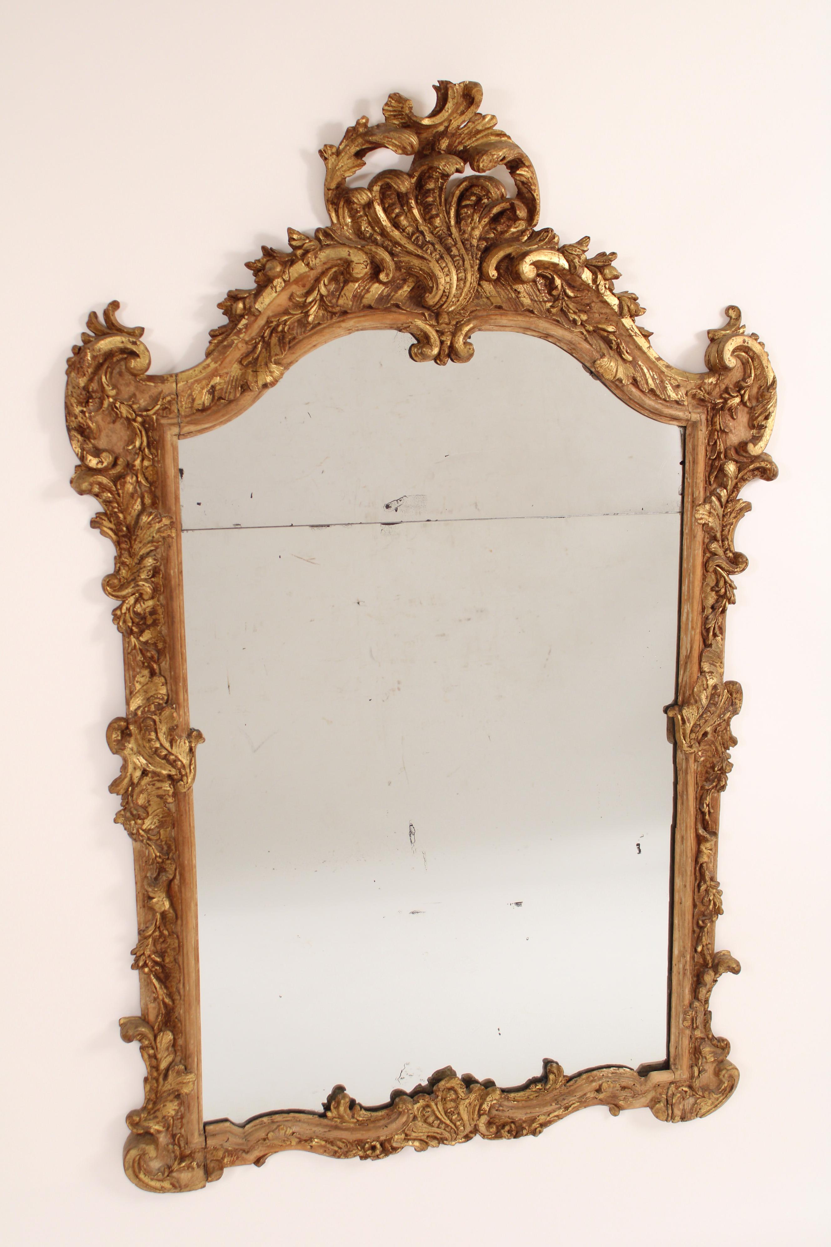 Miroir ancien de style Louis XV en bois doré, 19ème siècle. Avec un fronton sculpté de coquilles et de feuillages, des côtés sculptés de feuilles, la base du miroir sculptée de feuilles et de coquilles. Une partie importante de la dorure est