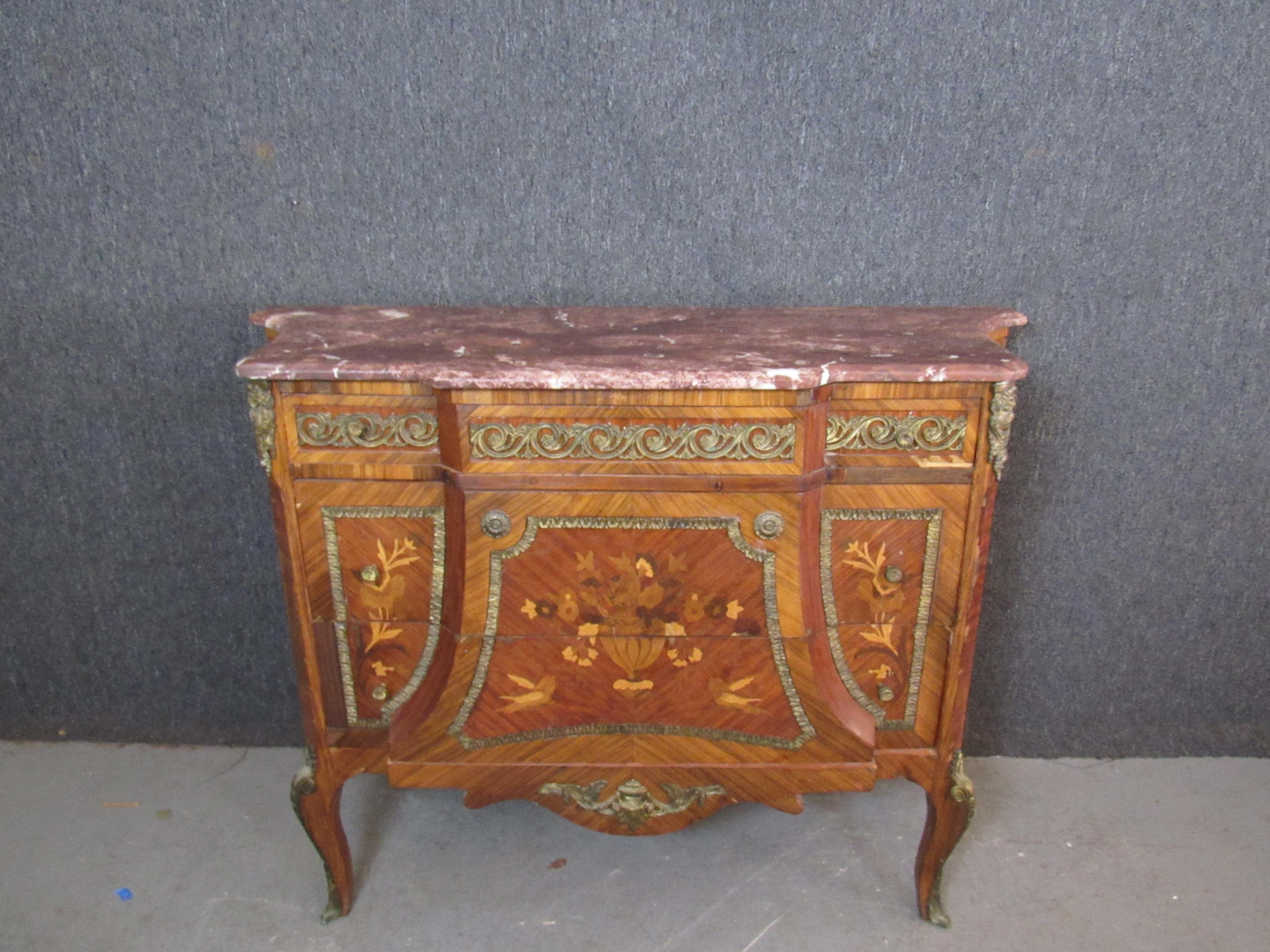Relieve all the magic and splendor of King Louis XV's royal court with this exquisite antique commode. A striking zebrawood veneer accentuates the beautiful marquetry of birds and flowers. Cast metal adornments give a sense of timeless luxury. A