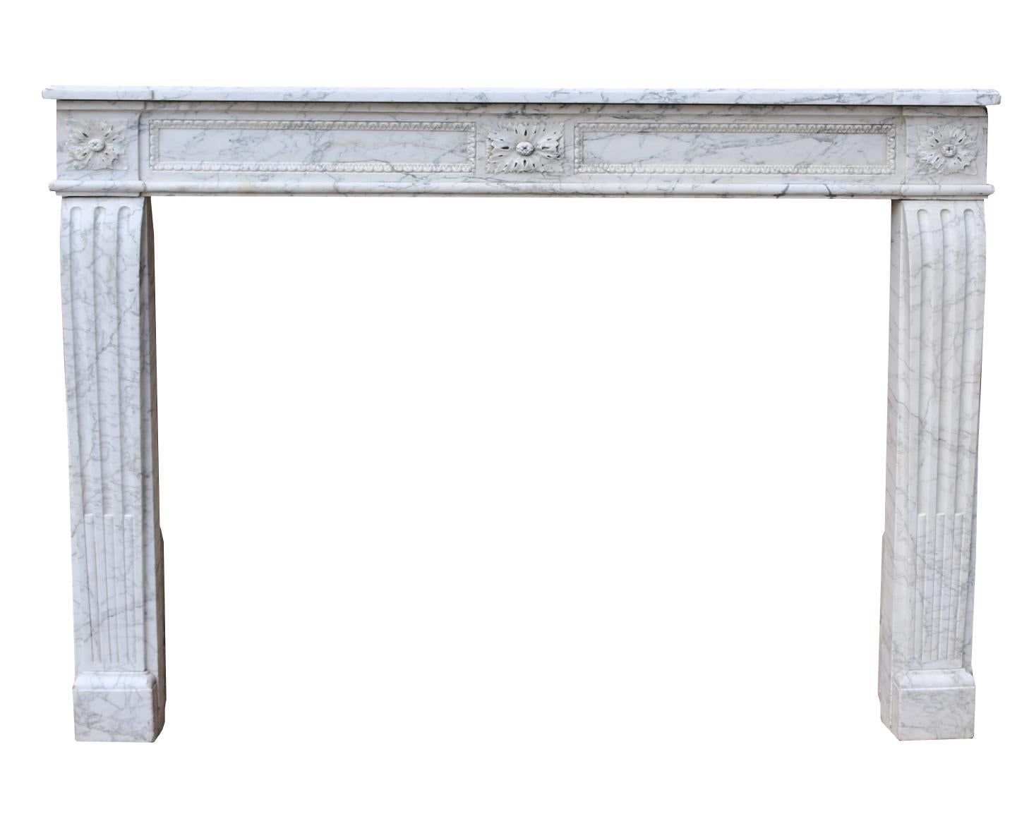 A Louis XVI fireplace surround in Carrara marble, with a floral paterae centred on the panelled frieze and echoed on the end blocks which are set above stop fluted jambs resting on small foot blocks.

Additional dimensions:

Opening height 95.5