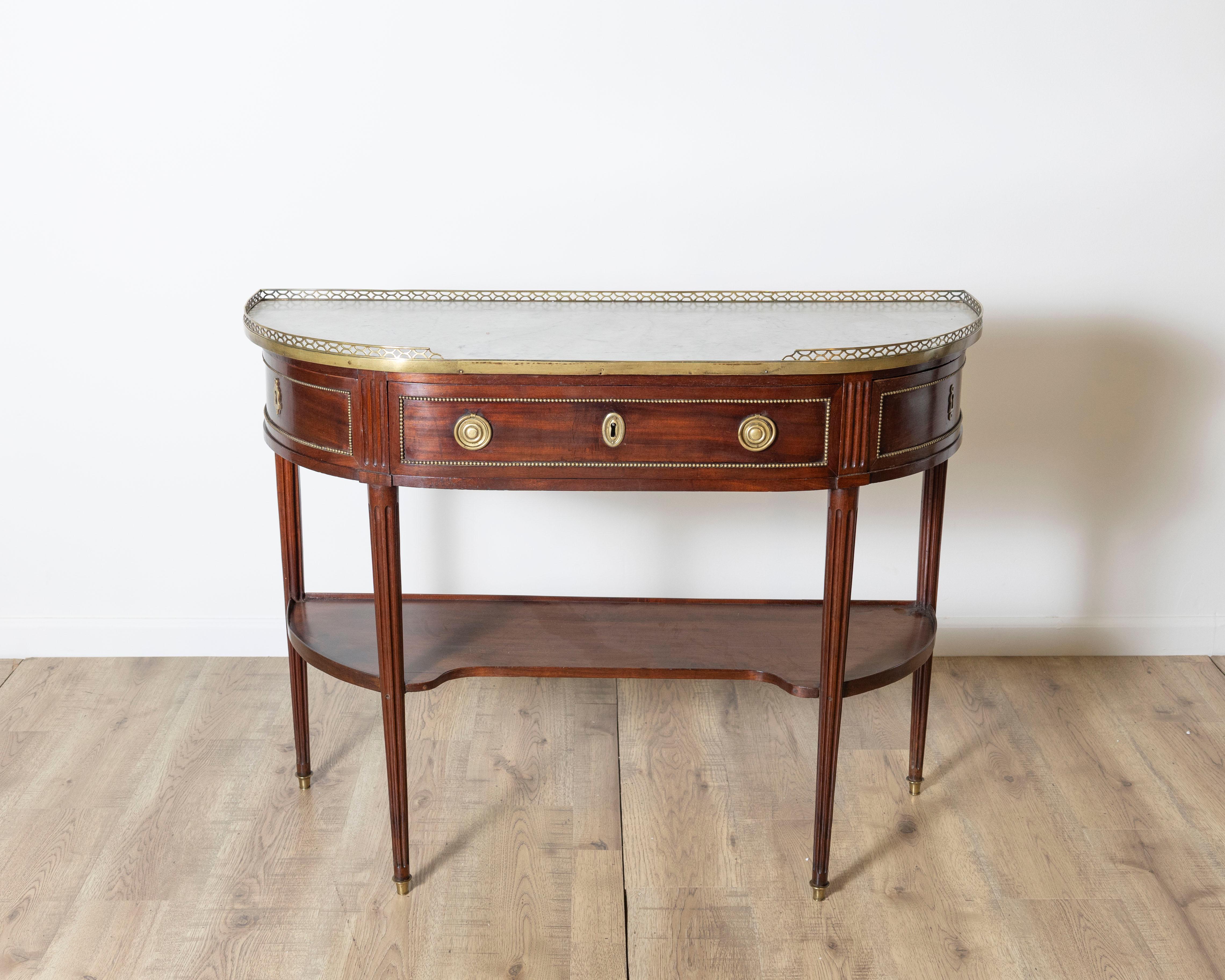 Un'elegante consolle in stile Luigi XVI dell'inizio del XIX secolo realizzata in pregiato mogano con raffinate linee neoclassiche e squisiti dettagli. La forma demilinea è sormontata da una superficie sagomata in marmo di Carrara, incorniciata da