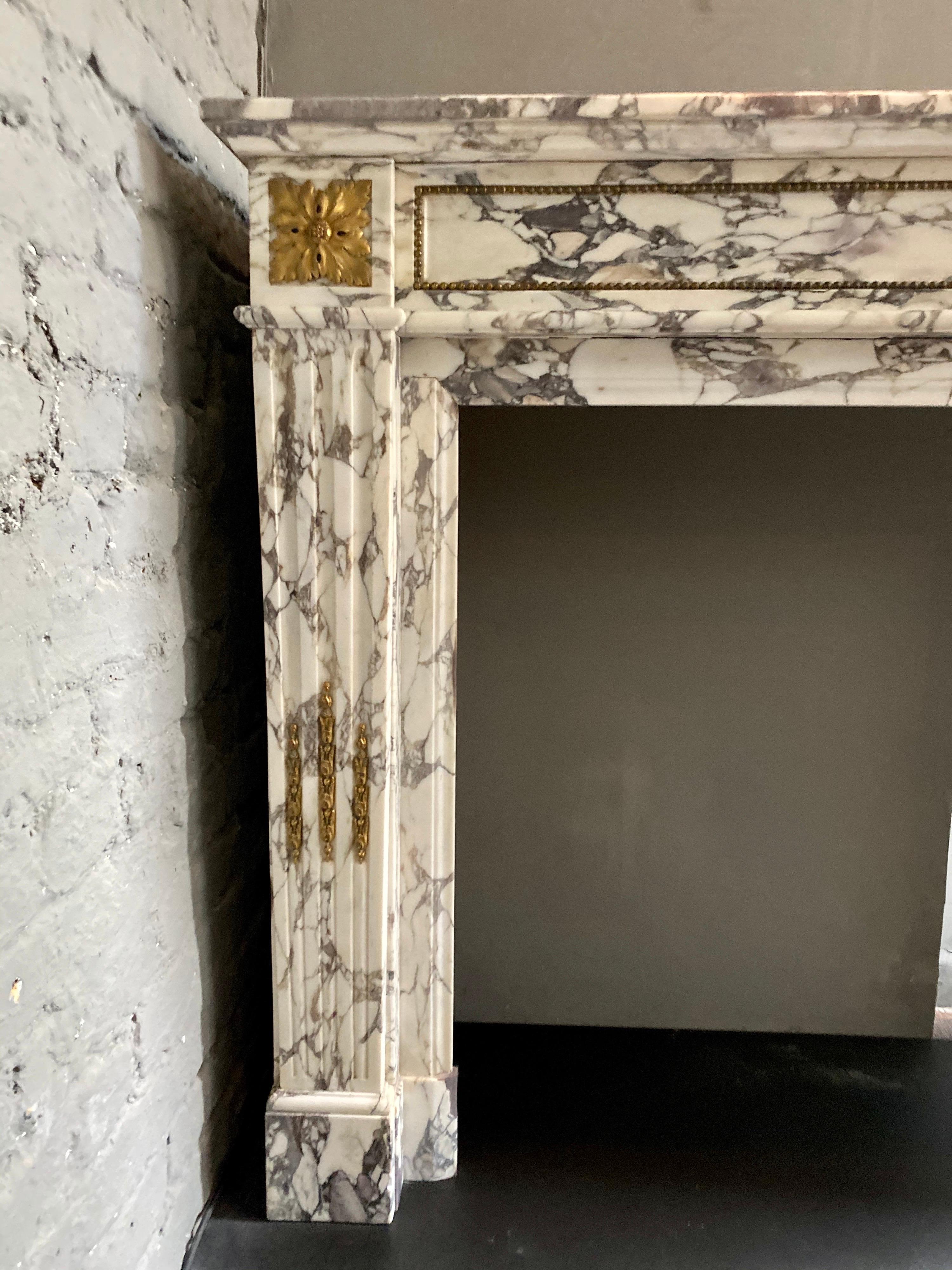 A superior quality antique French surround in rare Breche Violette marble, with Ormolu mounts. The stop fluted jambs with Ormolu Husks and surmounted by Ormolu Patarae. The panelled frieze with beaded Ormolu running the length. A wide moulded inner