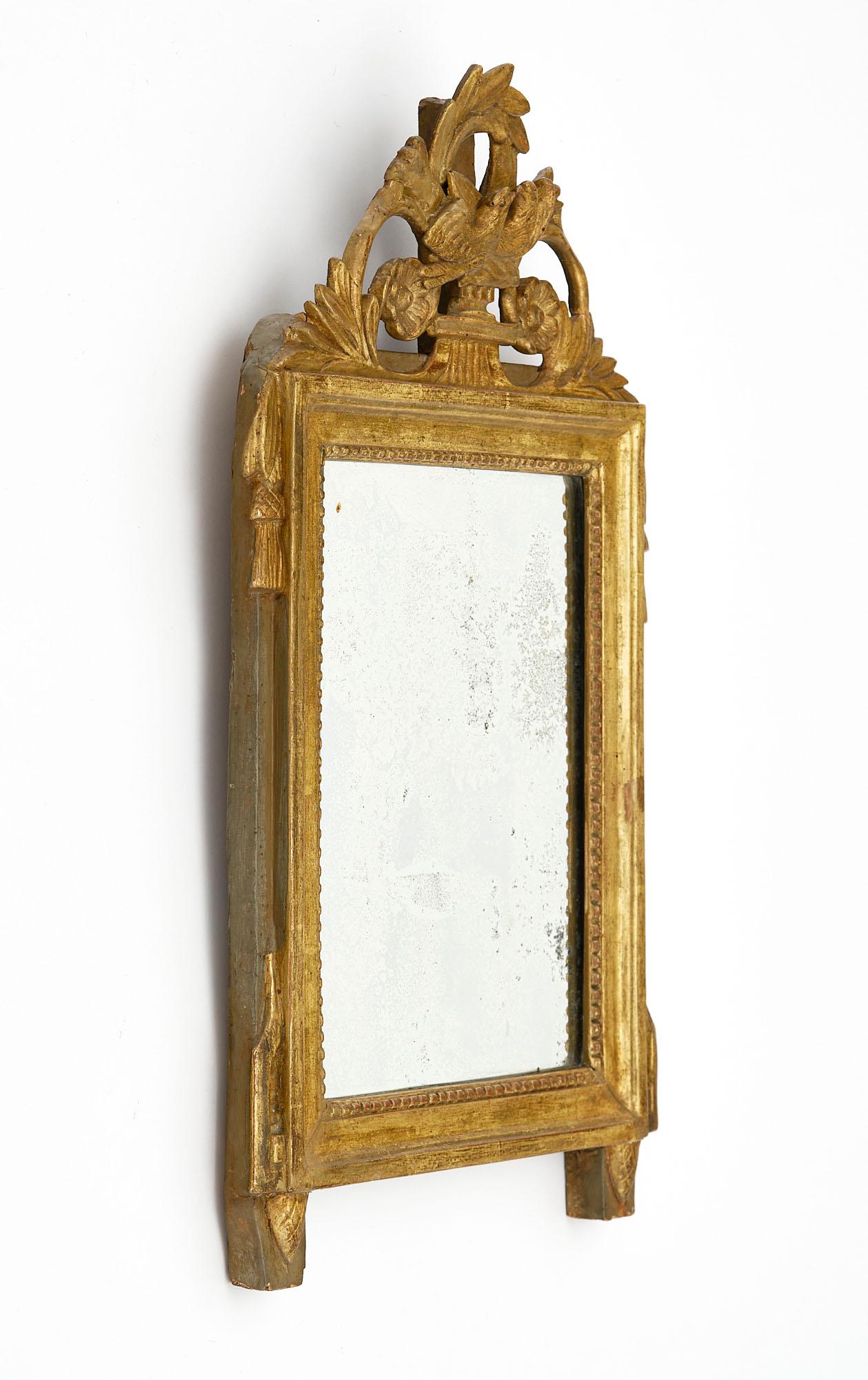 Miroir de France d'époque Louis XVI. Cette pièce est en bois stuqué et sculpté à la main, avec un fronton représentant des oiseaux, des motifs floraux et une couronne de laurier. Les feuilles d'or 24 carats sont d'origine, de même que le miroir au
