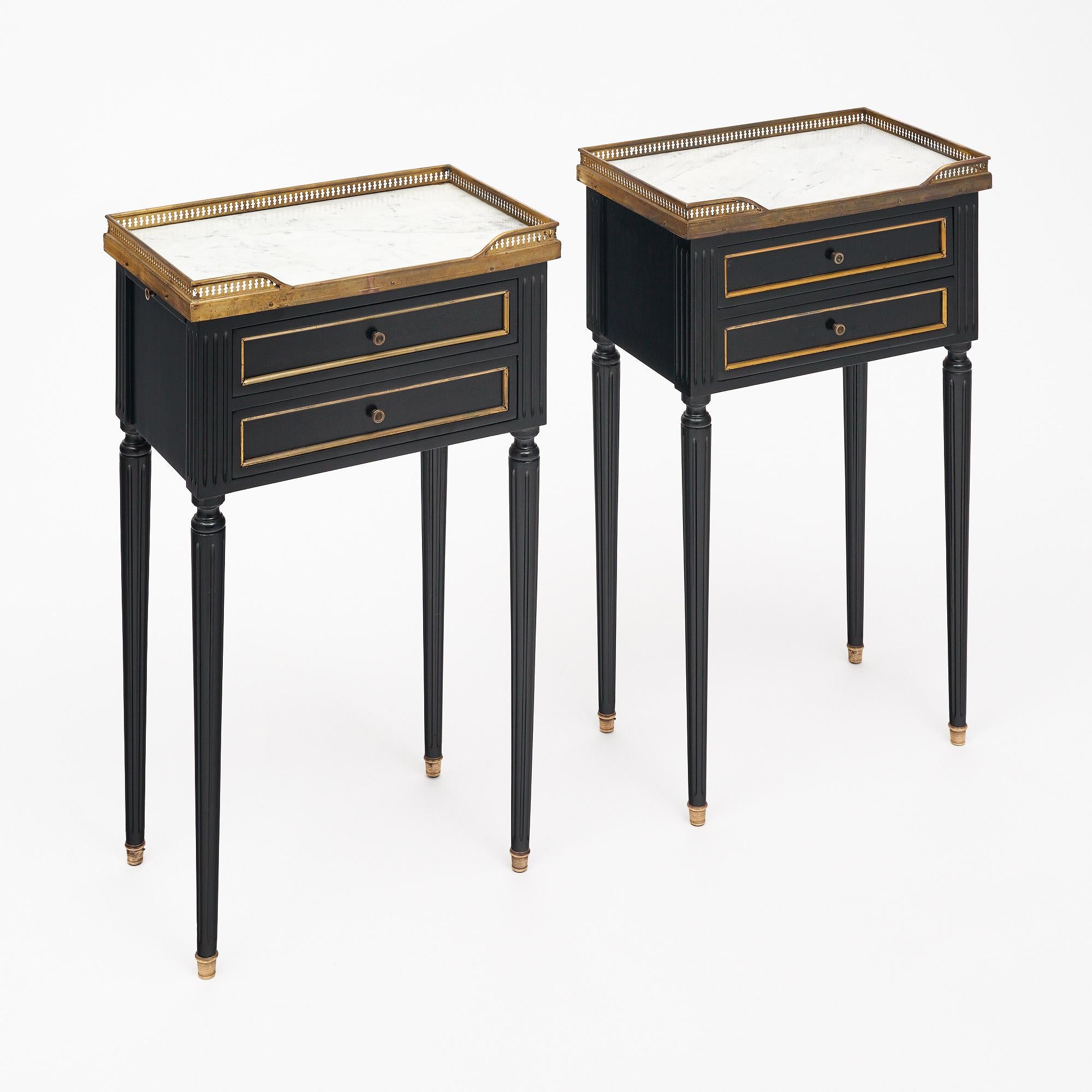 Paire de tables d'appoint de style Louis XVI en France. Cette paire est ébonisée et finie avec un poli français lustré de qualité muséale. Chaque table comporte deux tiroirs à queue d'aronde et est surmontée d'un marbre de Carrare entouré d'une
