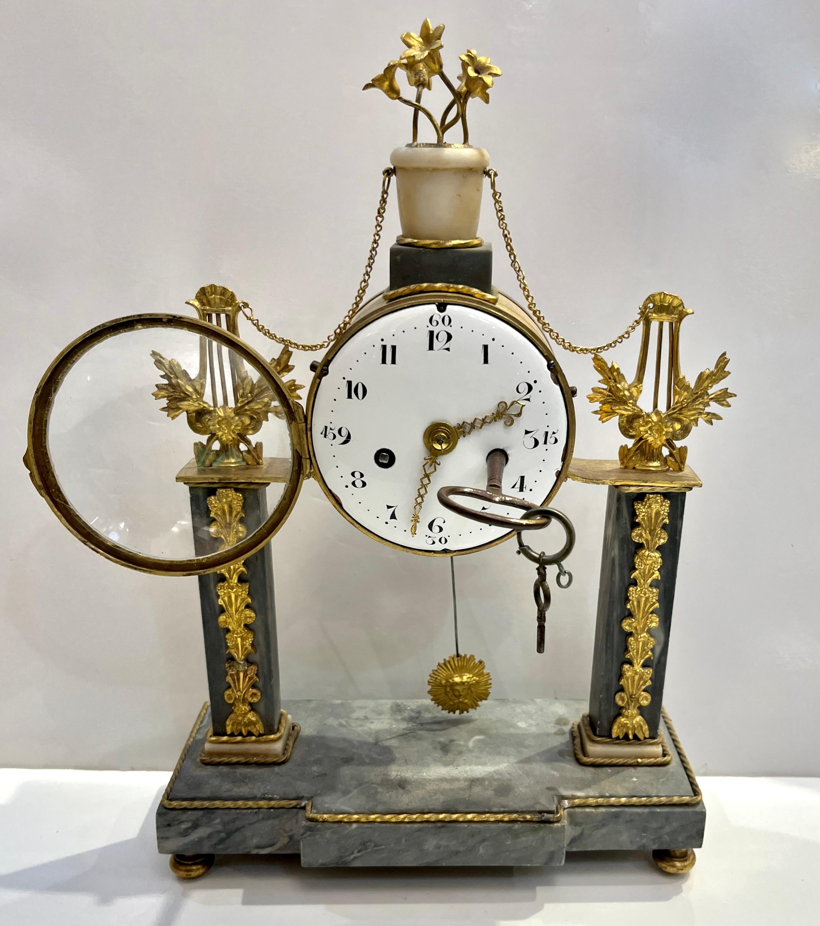 A refined and authentic Louis XVI period mantel clock, that still chimes, this exceptional late-18th-century timepiece features an elegant white enamel dial with Arabic numerals, suspended between two stately grey marble columns enriched with finely