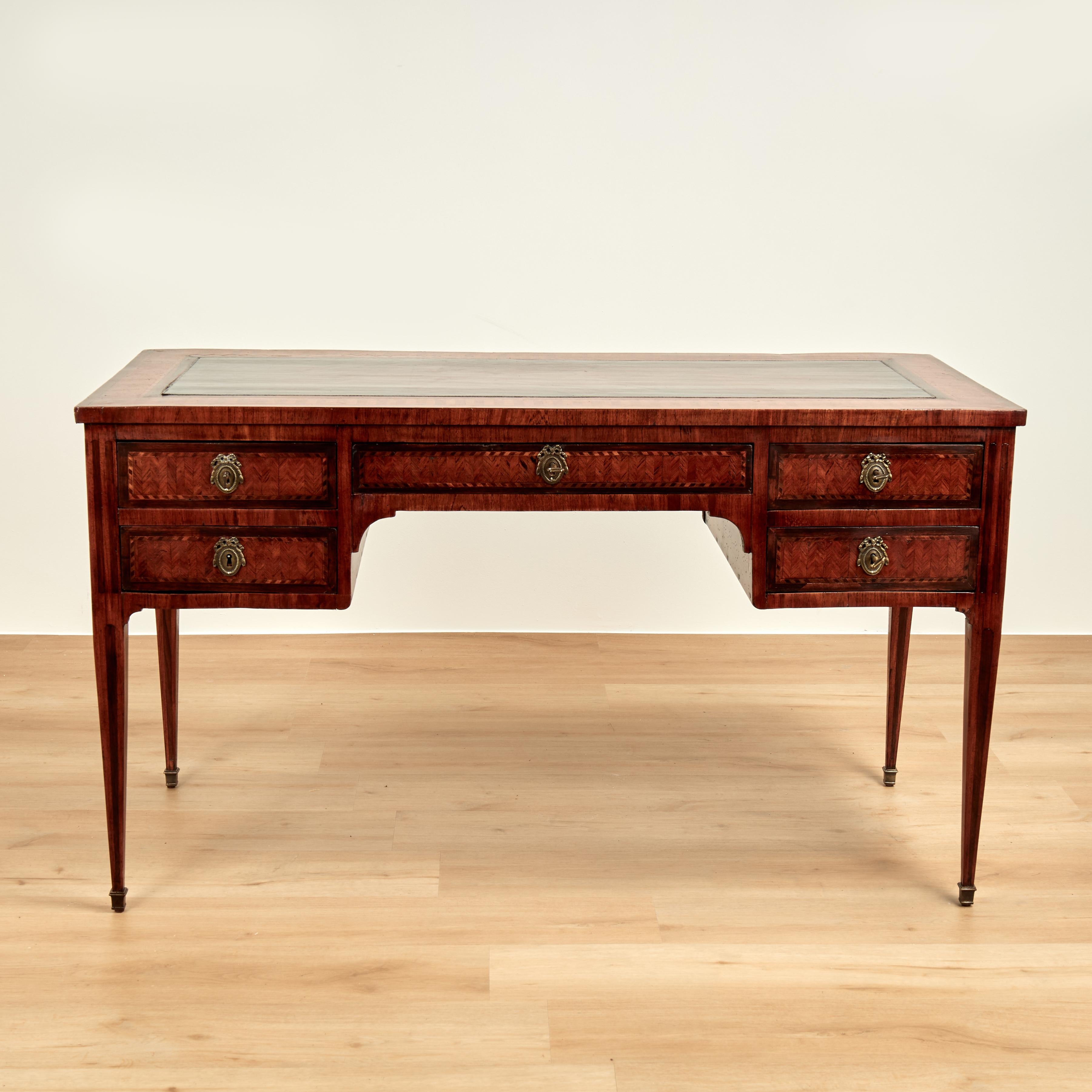 Handsome 18th century French desk handcrafted in mahogany and featuring a tooled leather top, chevron style inlays all around, five drawers in front and faux drawers on the reverse, brass hardware, keys and elegant tapered legs.
