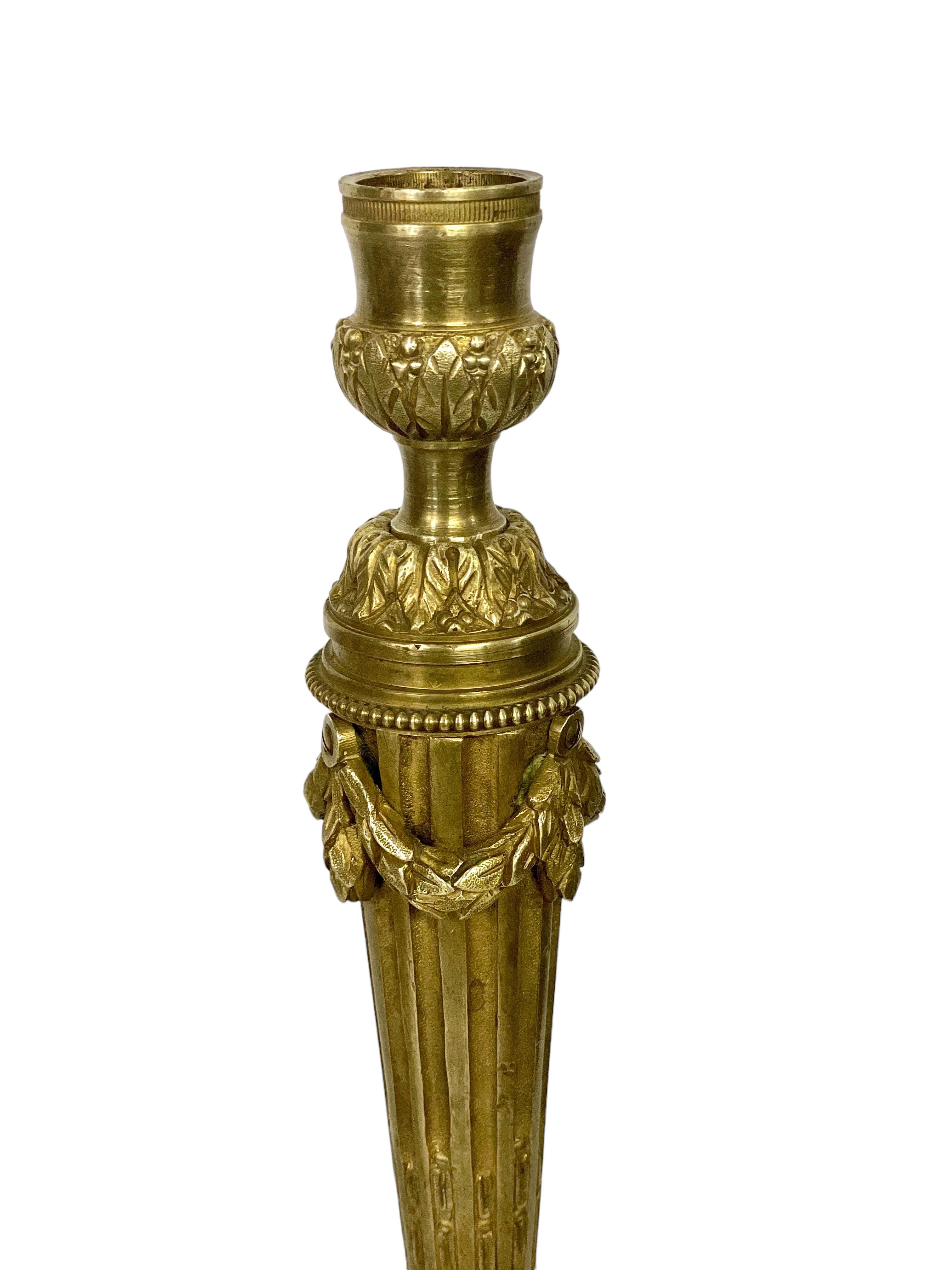 Une impressionnante paire de chandeliers de style Louis XVI en bronze ciselé et doré, datant du 19e siècle. Reposant sur de lourdes bases circulaires entourées de motifs de perles et de feuillages stylisés, les fûts des colonnes sont effilés et