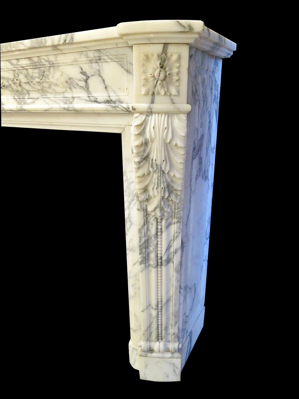 A large and well proportioned French antique fireplace in rich Italian Arabescato Marble in the Louis XVI manner. The bowed front frieze with carved bow tied Laurel leaf, flanked by square carved Patarae corner blocks. The Jambs with console canted