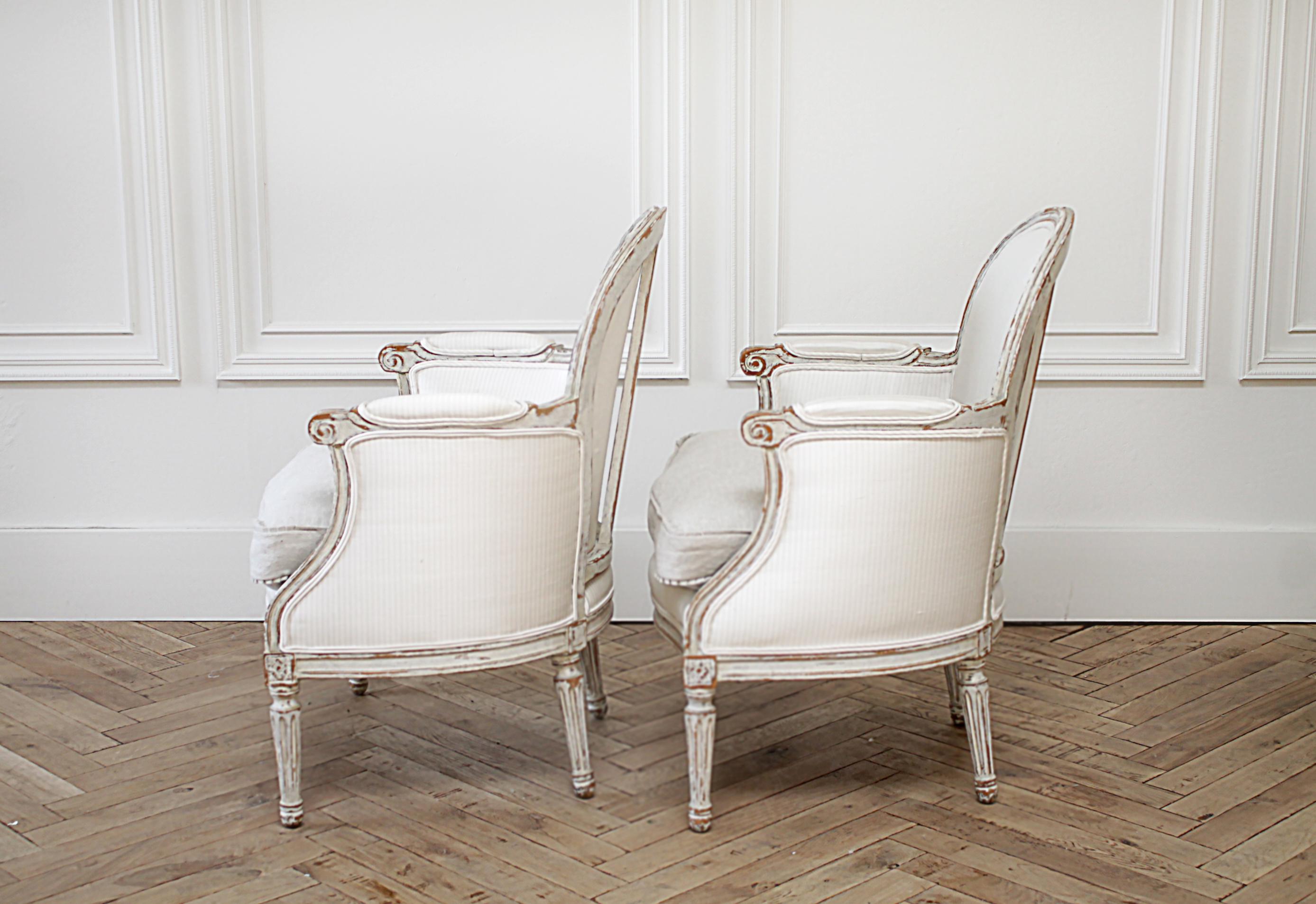 Antique Louis XVI style bergère chairs in silk and linen upholstery.
Original creamy painted patina with bare wood showing through. We reupholstered these in a neutral tonal stripe 100% silk, and linen slip covered seat cushion. The seat cushion