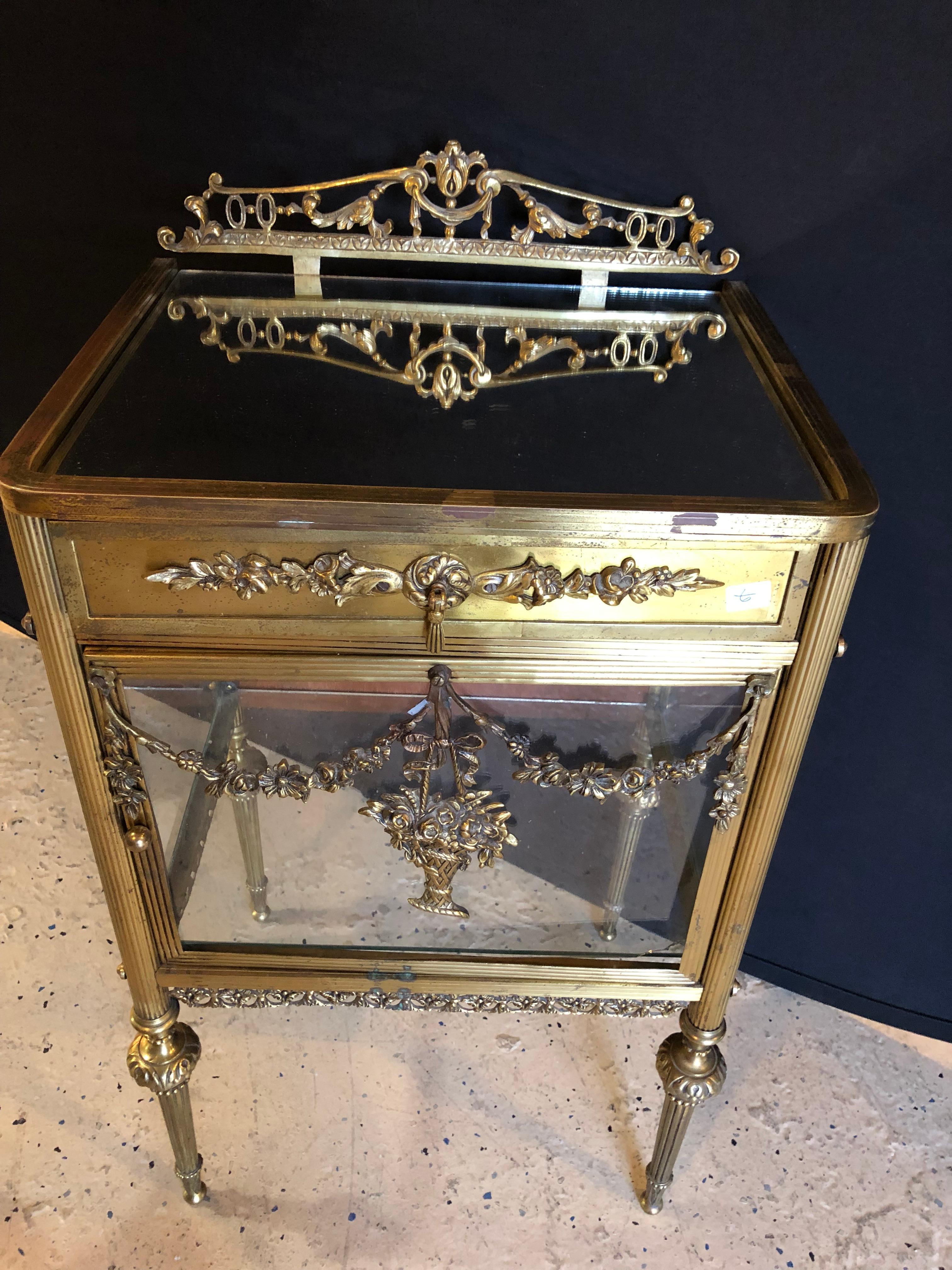 This early antique Louis XVI style bronze / glass vitrine cabinet or nightstand is simply stunning and constructed of the finest quality. The bronze mounts of Fine form with a single drawer over an open glass and mirrored vitrine cabinet. The front