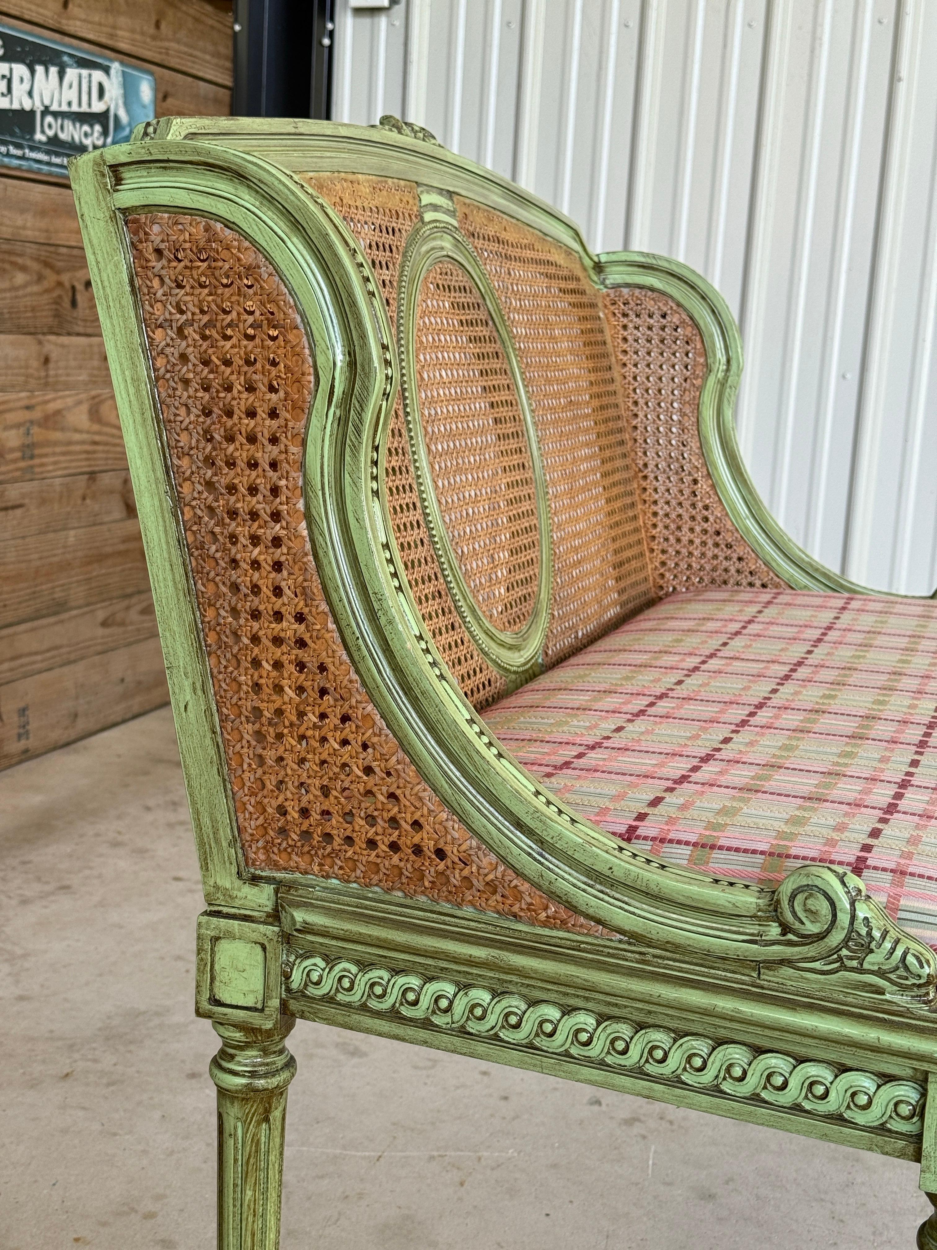  charming antique Louis XVI style caned settee featuring a hand-carved wood frame in a distressed green painted finish.
The medallion back and sides are finely caned, paired with a colorful plaid upholstered seat that has been previously redone and
