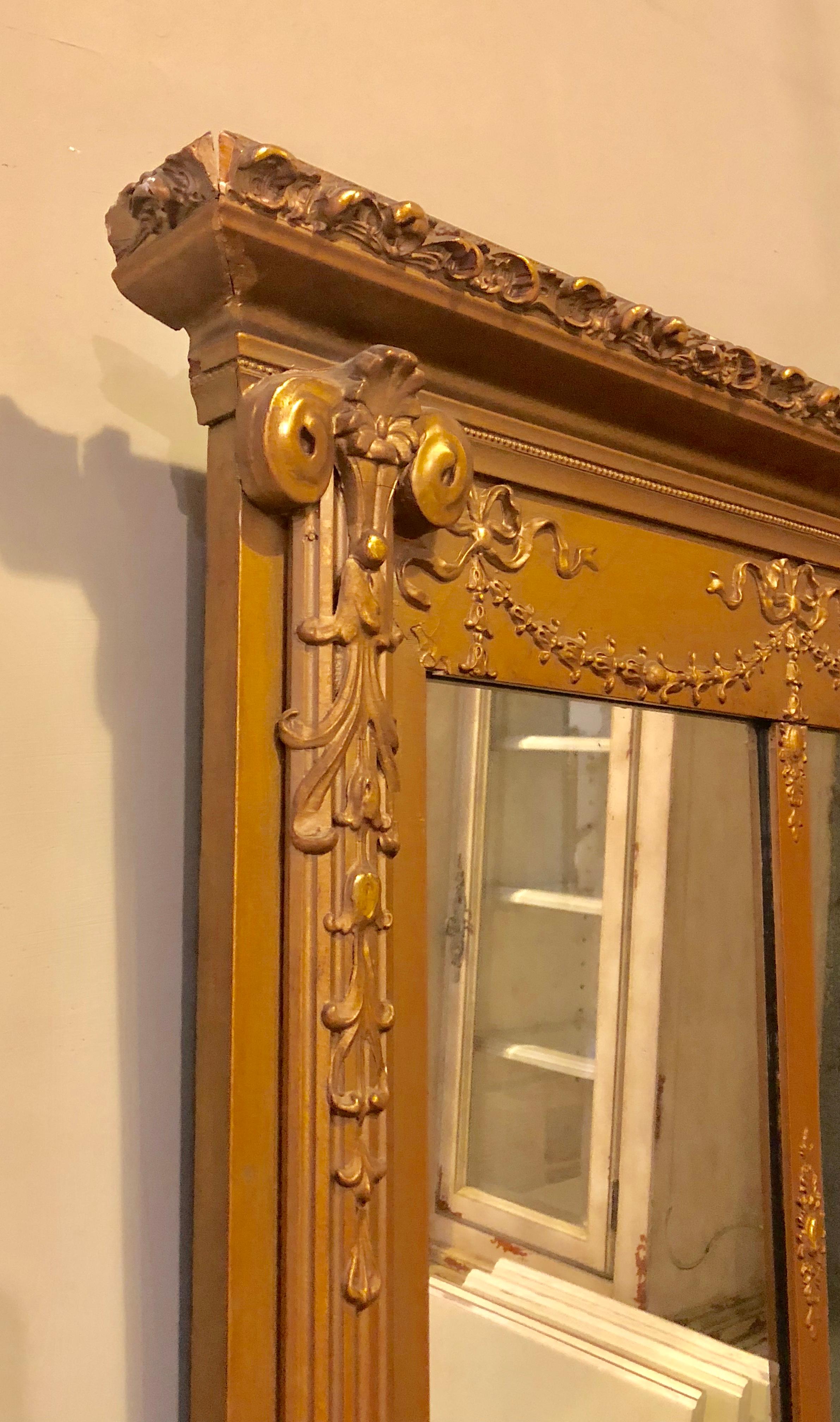 An antique Louis XVI style carved giltwood over the mantel mirror. This finely gilt over the mantel or console mirror has three panels flanked by column-form carved sides with a carved swag apron. The mirror itself with a clear center. The frame