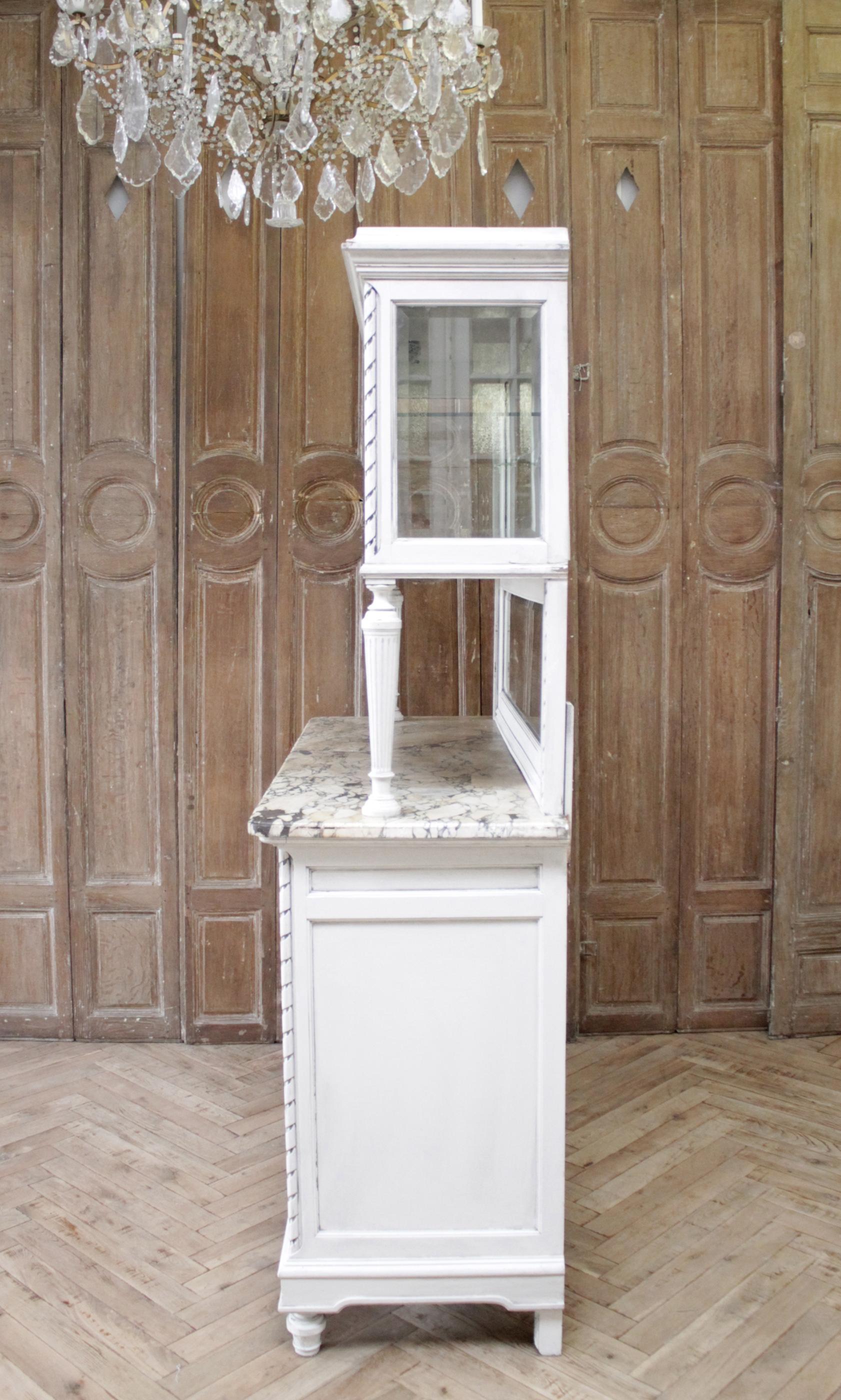 Antique Louis XVI style China cabinet with marble top
Painted in our oyster white finish, with subtle distressed edges, and antique patina, the finish has a slight grayish tone. Lovely delicate ribbon and rose swag carvings are on the doors, and