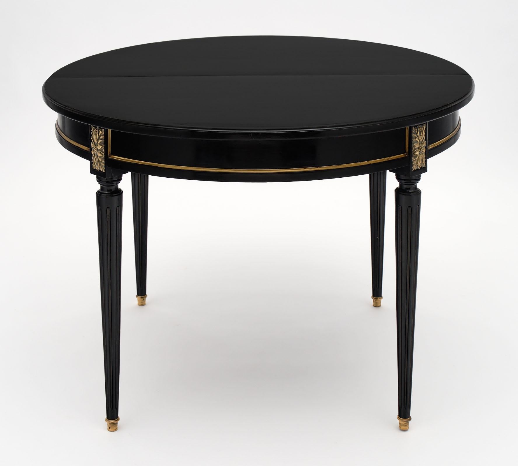 Round Louis XVI style antique dining table made of mahogany that has been ebonized and finished with a French polish. There is gilt brass trim and details throughout. We love the tapered legs with fluting and the bronze feet. The table opens up and