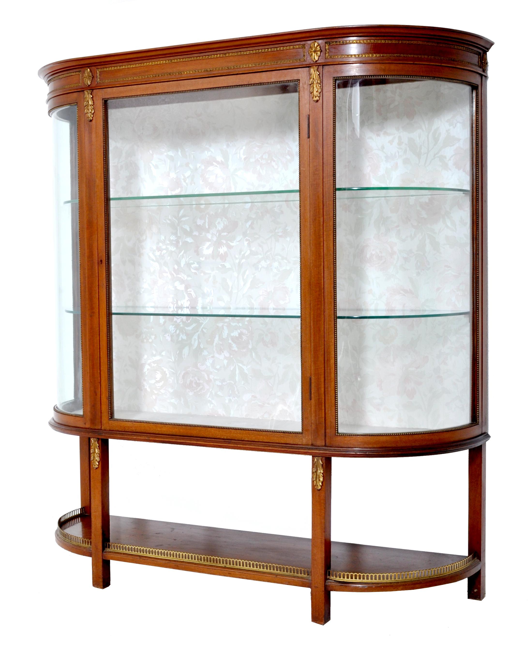 Antique Louis XVI style English mahogany curved China display cabinet, circa 1890. The cabinet having gilded bronze mounts and oval gilded bronze paterae to the top, below having corresponding gilded bronze acanthus leaves. The cabinet having a