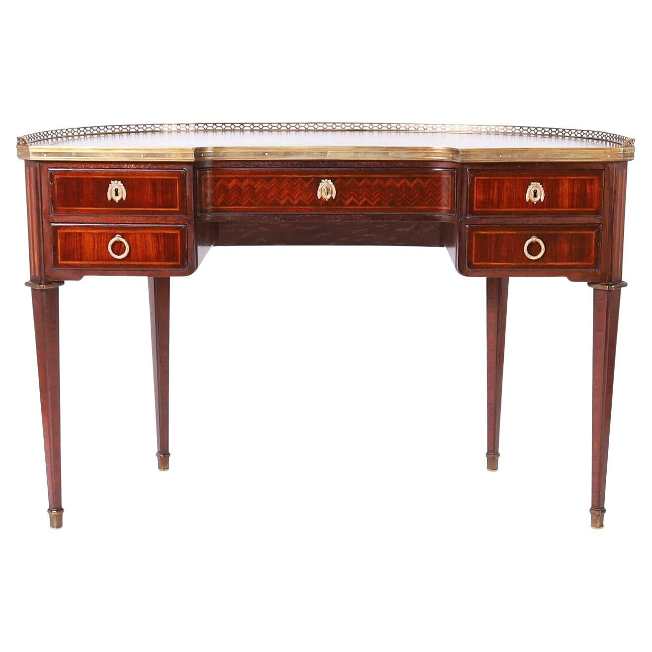 Fine antique Louis XVI style desk crafted in mahogany and kingwood featuring a tooled leather top with a cross banded border and brass gallery. The case has five drawers decorated with inlays and cross banding and sits on elegant tapered legs with