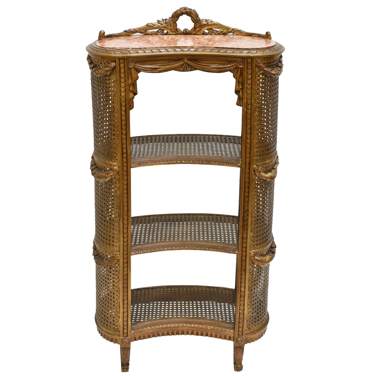 A lovely French étagère in the Louis XVI style in the form of a kidney with caning on the rounded sides and on the three shelves which are all painted using a gold saturated varnish in a burnished gold/ bronze color. The top is inset with a