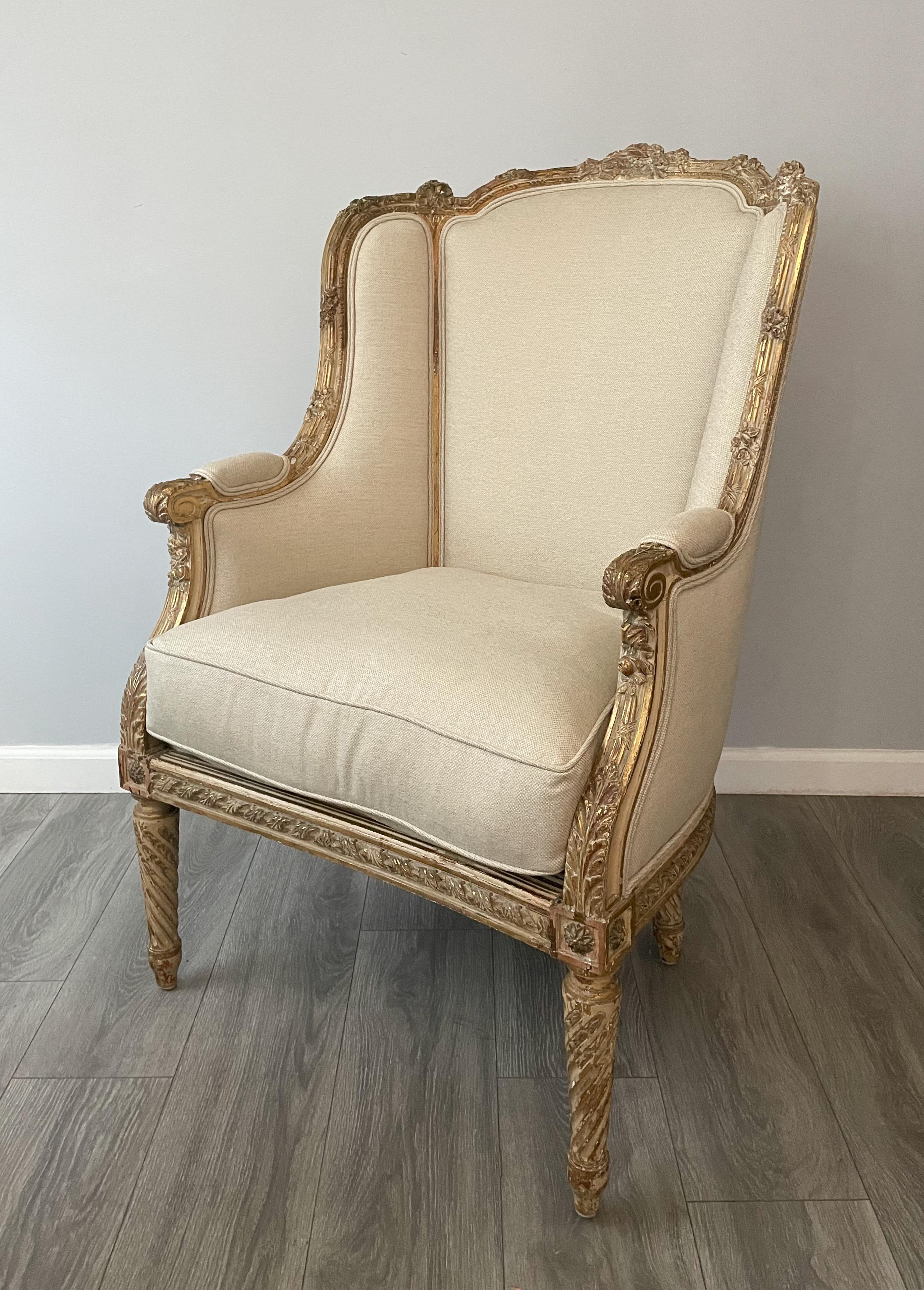 Fine, French 19th century carved bergère in the Louis XVI-style.

The chair features intricately carved decorations, a naturally distressed painted and parcel-gilt finish. New cotton linen upholstery with a loose goose down seat cushion and