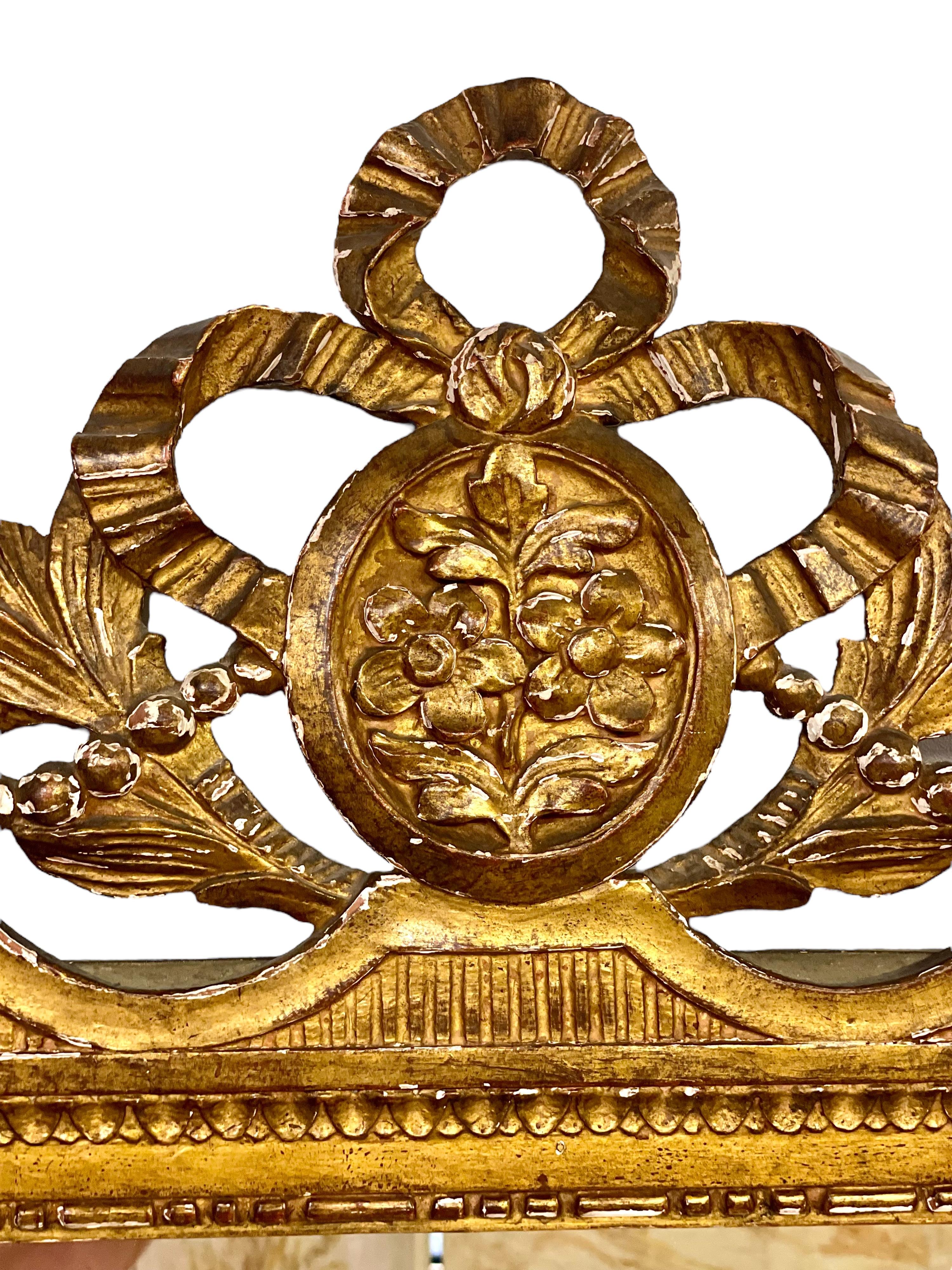 Favoloso specchio da parete in legno dorato intagliato della fine del XIX secolo, con frontone coronato da un motivo a nastri annodati che circonda un medaglione floreale ovale e affiancato da ramoscelli di acanto e fiori di cardo. La cornice è