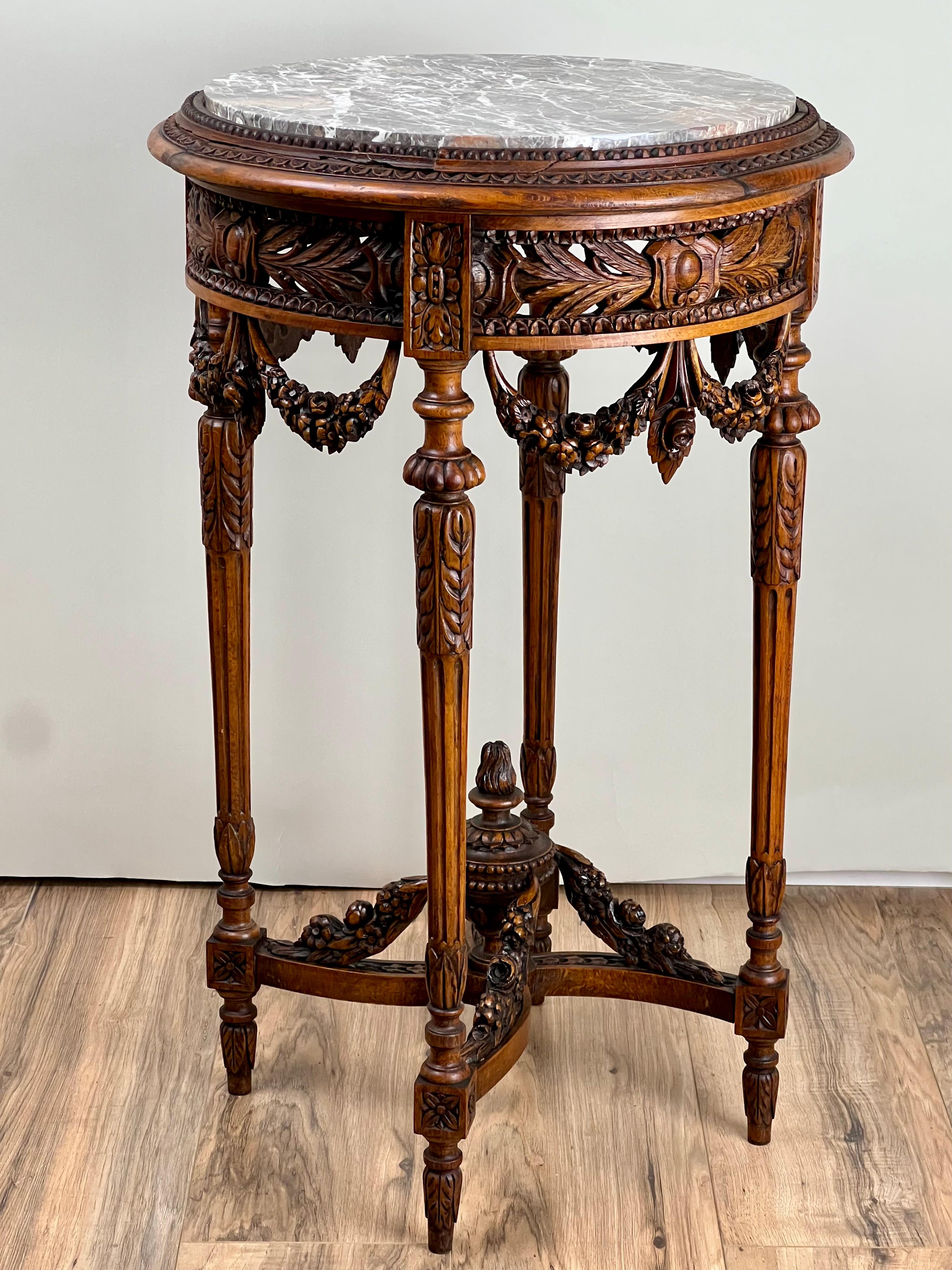 This elegant late 19th-century Louis XVI-style side table was hand-carved in Belgium, showcasing the refined neoclassical sensibility that defined the era. The round top features beautifully veined gray marble with a molded edge resting above an
