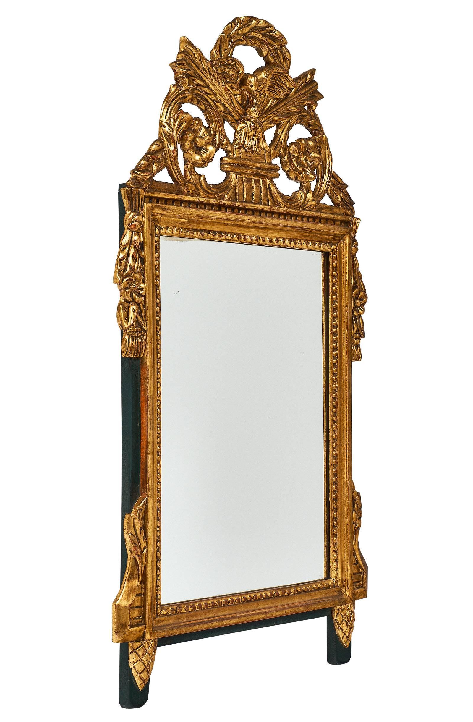 A French antique Louis XVI style mirror featuring hand-carved decor on wood of arrows, laurel crown, acanthus leaves, and florals. The mirror is covered in 23-karat gold leafing.