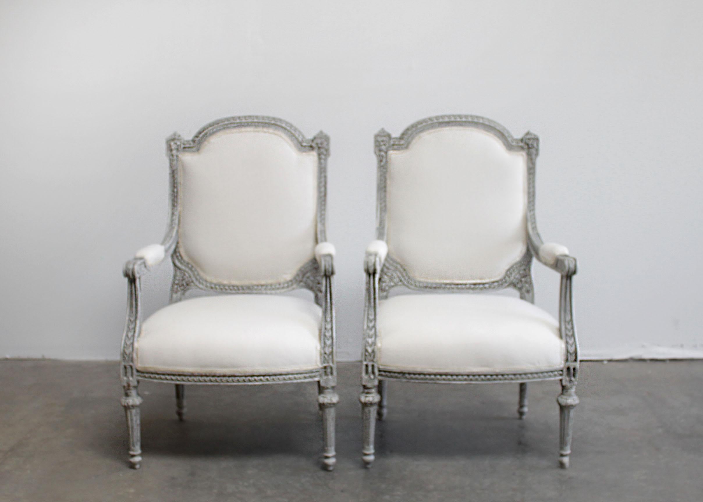 Antique Louis XVI style painted and upholstered carved open armchairs
Painted in a pretty gustavian gray finish with subtle distressed edges, and wood peeking through the paint.
Classic fluted legs, with medallion carvings atop the leg, and egg