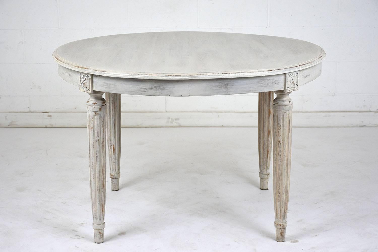This 1910s Louis XVI-style dining table is made of oak wood painted in an off-white and pale grey color combination with a distressed finish. There is a bevelled edge to the top of the table and carved floral accents along the table skirt. The legs