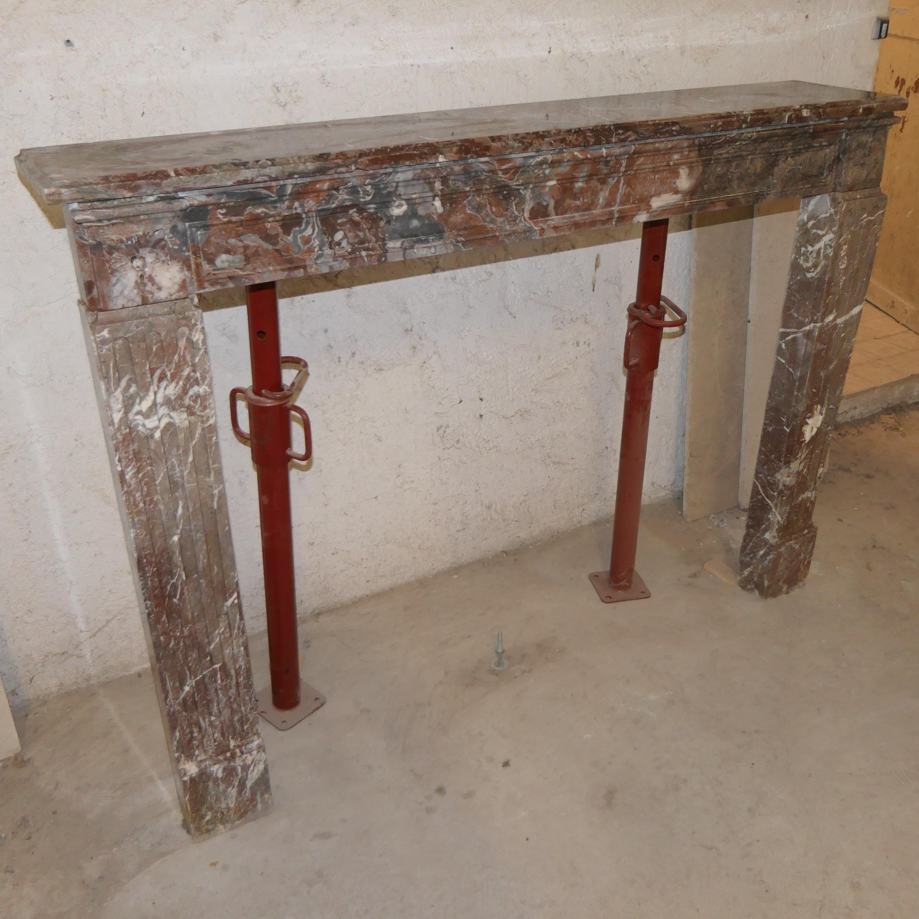 Questo magnifico caminetto è scolpito in un ricco marmo rosso (probabilmente Rouge Languedoc), caratterizzato da spettacolari venature bianche.

Il design, tipico dello stile Luigi XVI, è caratterizzato da un architrave dritto sostenuto da due