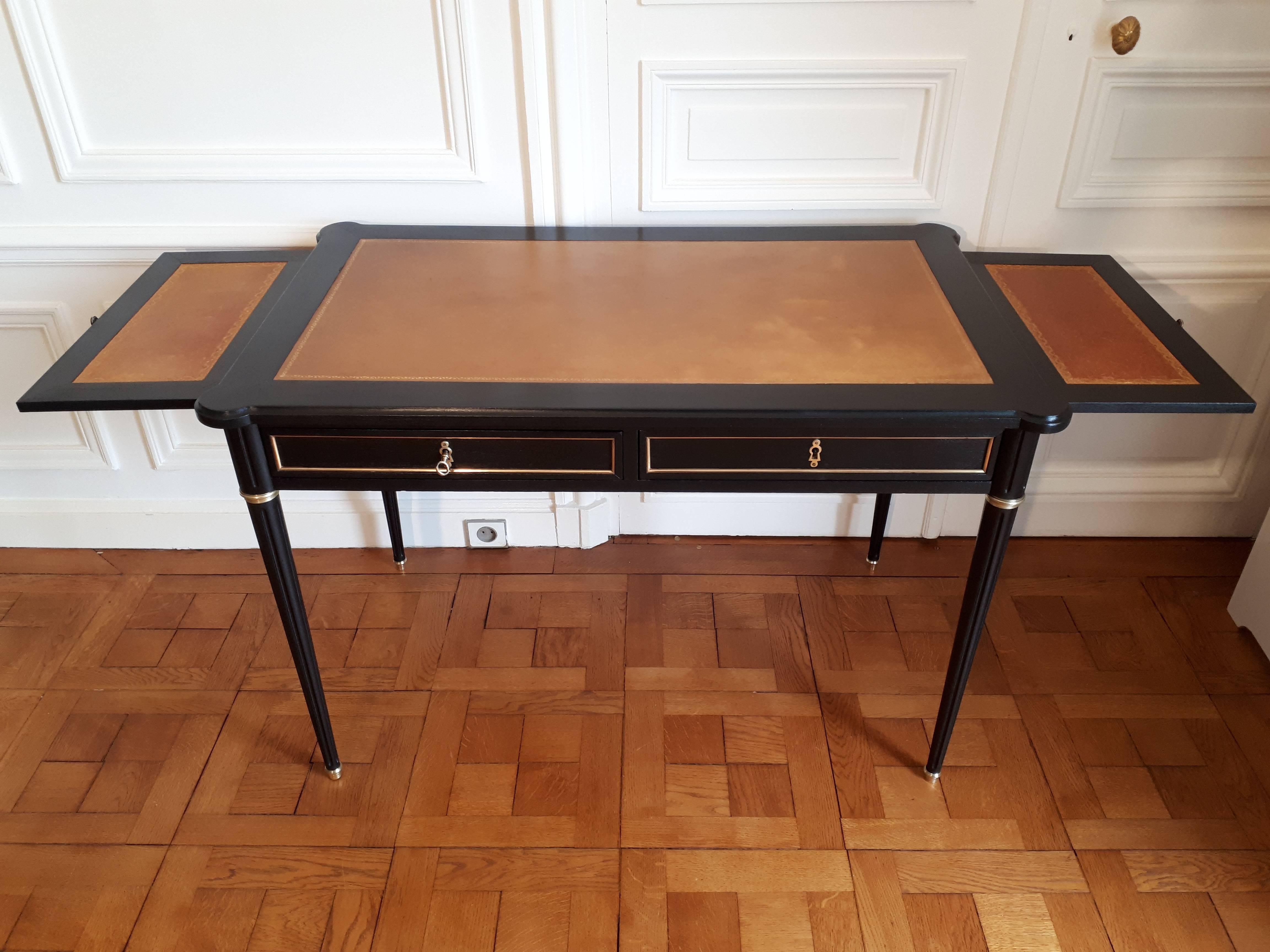 Antique Louis XVI style desk with cognac leather top and gold embossed frieze. The front of the room has two drawers with brass trim. The other three sides also have brass trim details, and each end has a sliding tray with matching cognac leather