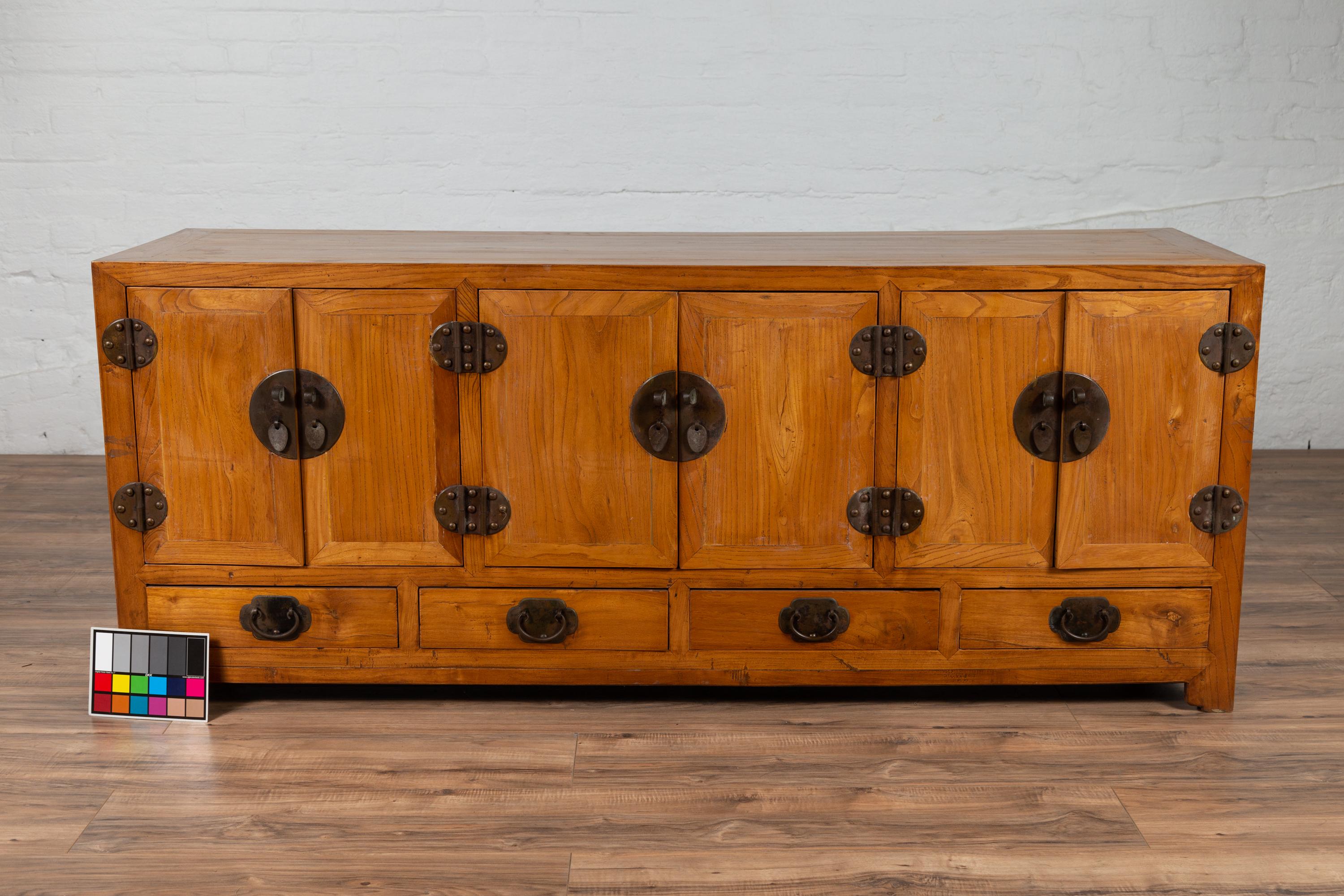A Chinese elm low Kang cabinet from the 19th century, with three sets of double doors and four drawers. Born in China during the 19th century, this low Kang cabinet features three sets of double doors sitting above four lower drawers. Each pair of