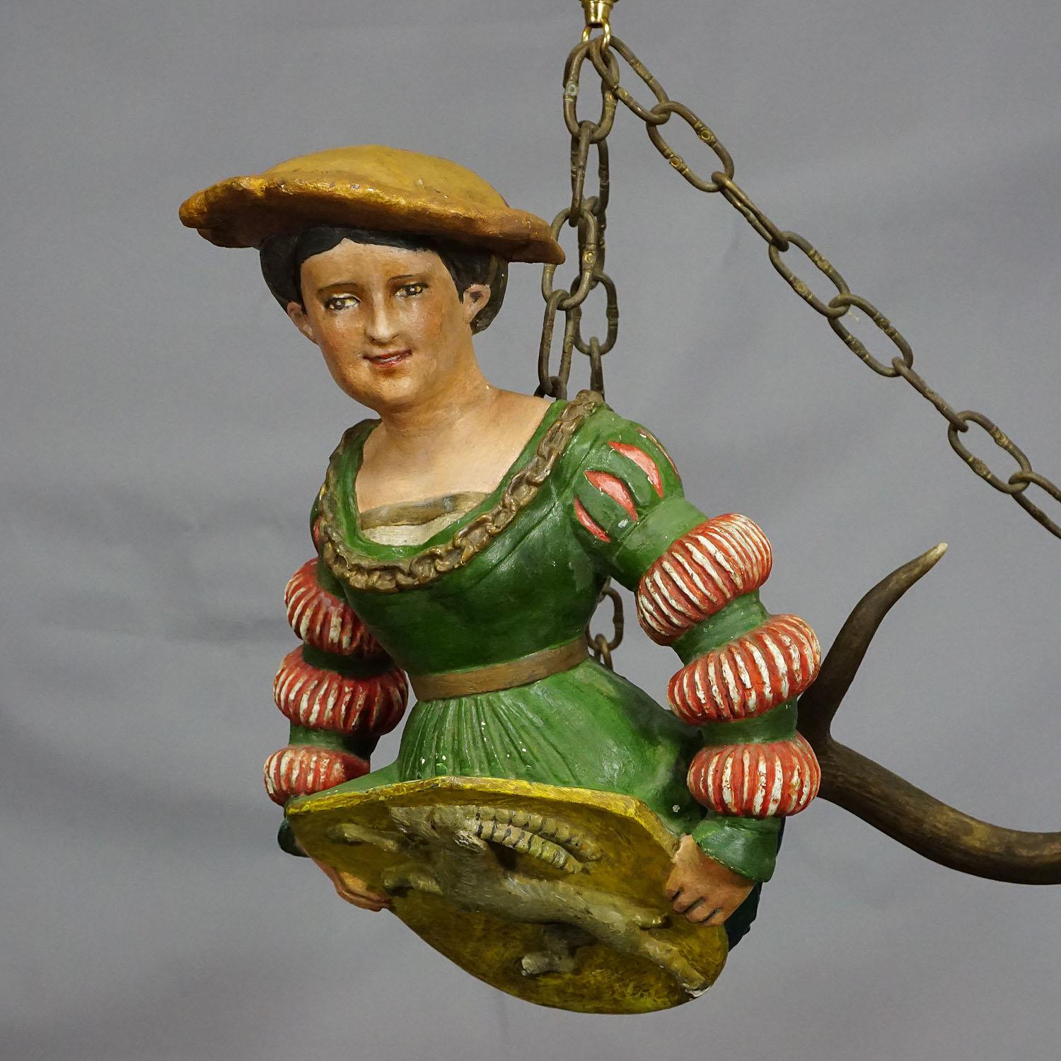 An antique lusterweibchen of a Victorian lady holding a hatchment which depicts an ibex relief. The statue is made of plaster and hand painted. Attached to a pair of original fallow deer antlers and a brass suspension. Good condition, painting