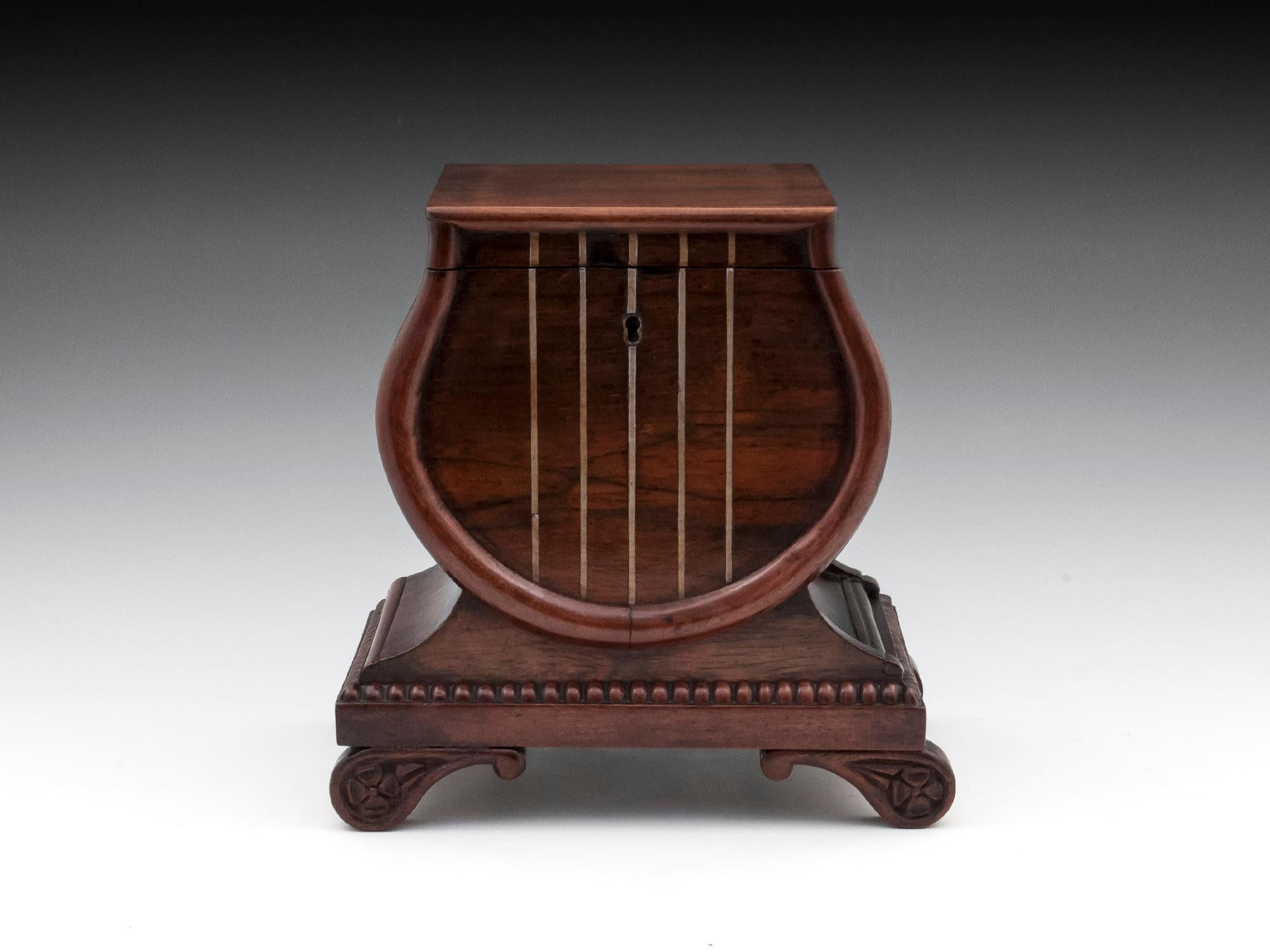 Unusual mahogany tea caddy in the form of a lyre with pewter strings.
The plinth base has a secret spoon drawer and stands on ornate, shaped feet.

The interior of this lyre tea caddy has a single rosewood lid covering two-foil lined