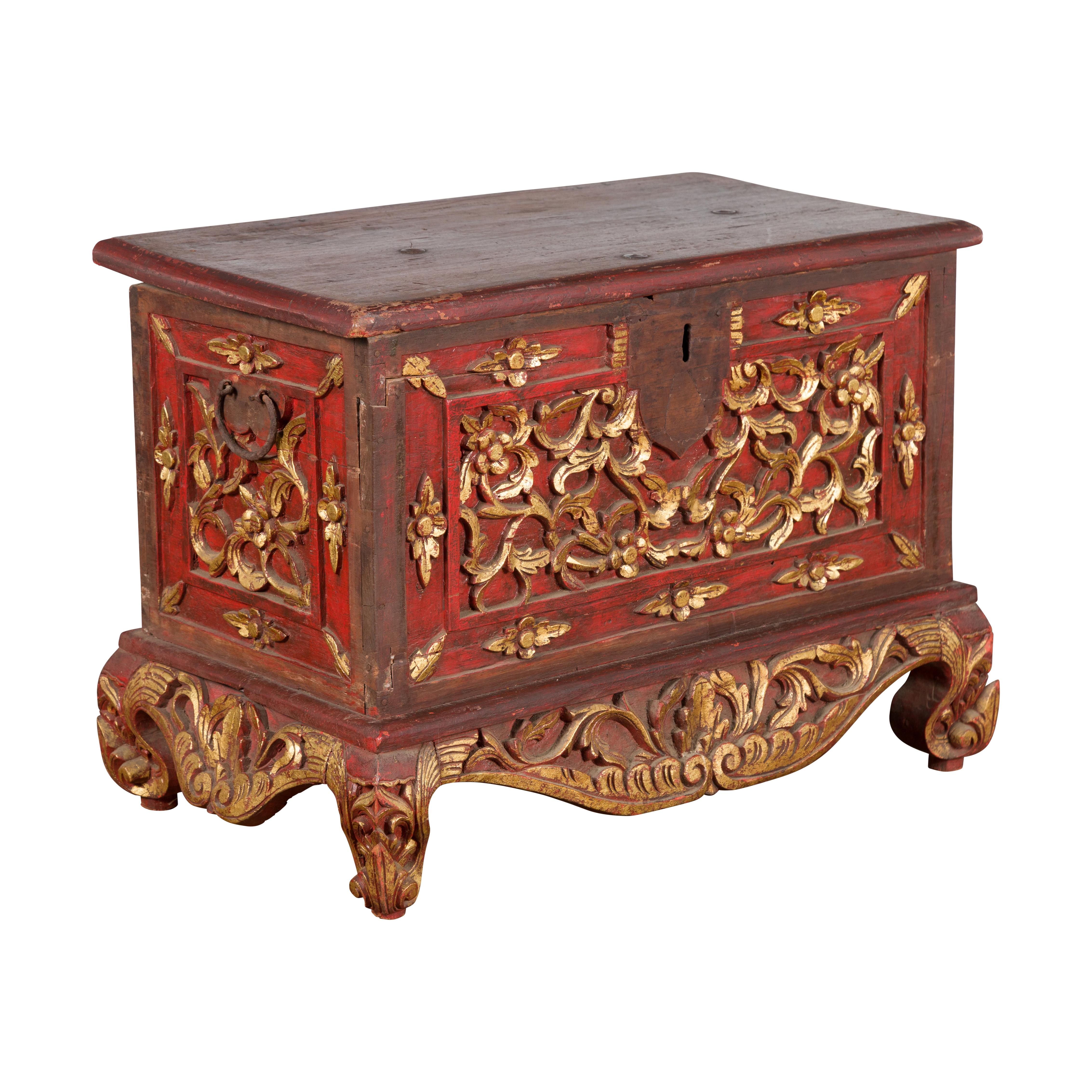 An antique Indonesian floral carved wooden treasure chest from the early 20th century, with red and gold accents. Created on the island of Madura off of the northeastern coast of Java, this treasure chest attracts our attention with its contrasting